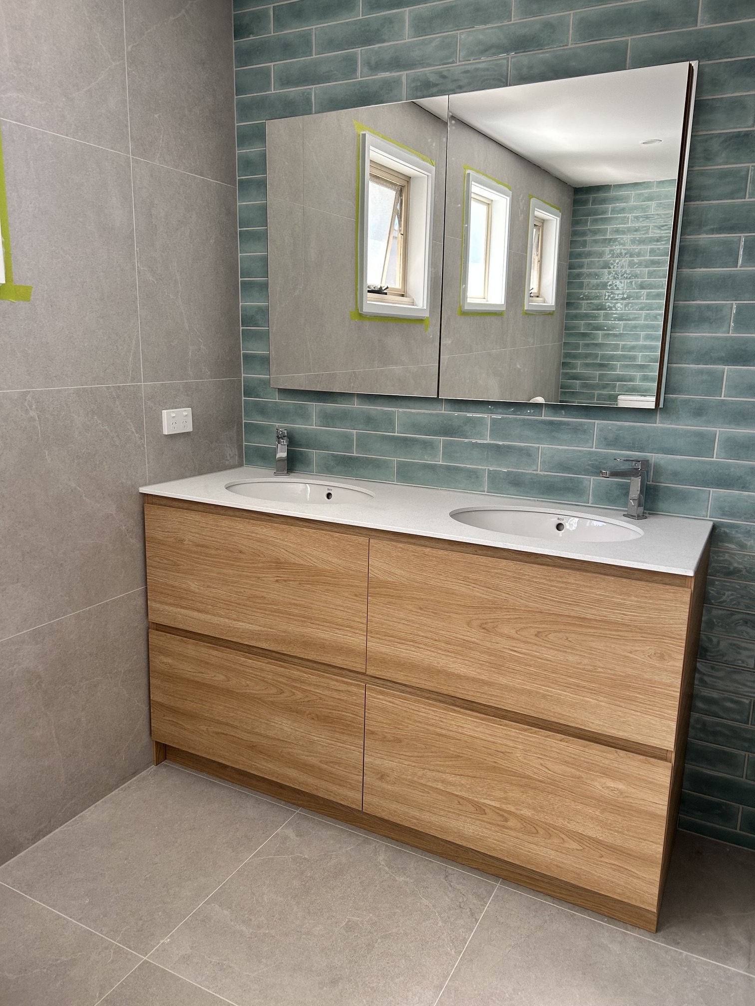 Modern bathroom vanity with double sinks, wood cabinetry, teal subway tile backsplash, and large mirrored cabinet