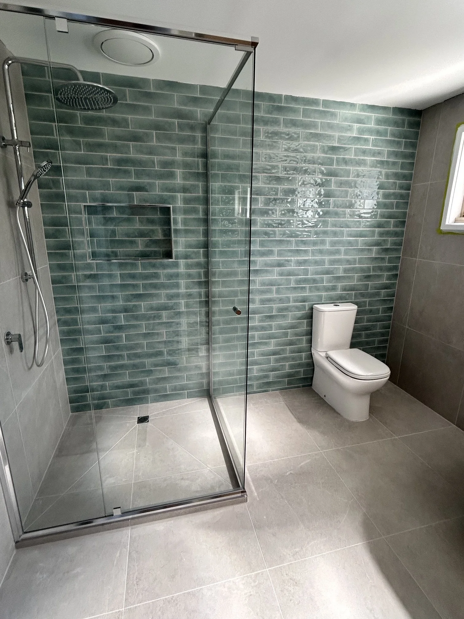 Modern bathroom with a glass-enclosed walk-in shower, green subway tile walls, and white toilet