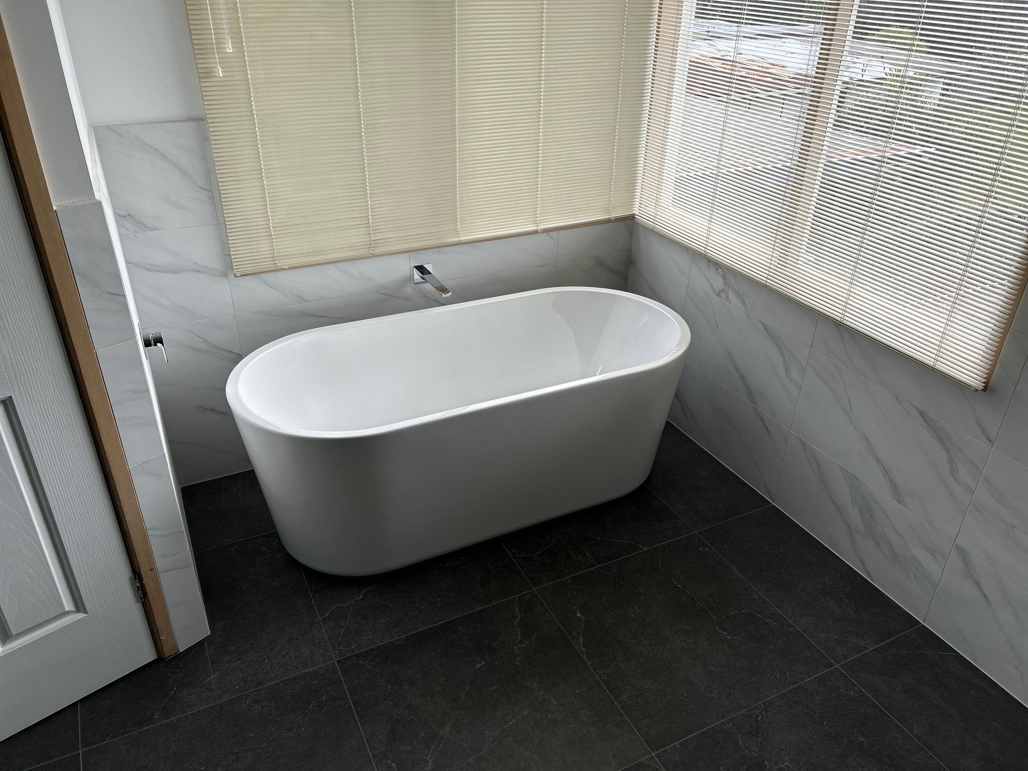 Modern bathroom with a freestanding white bathtub, marble-effect wall tiles, black floor tiles.