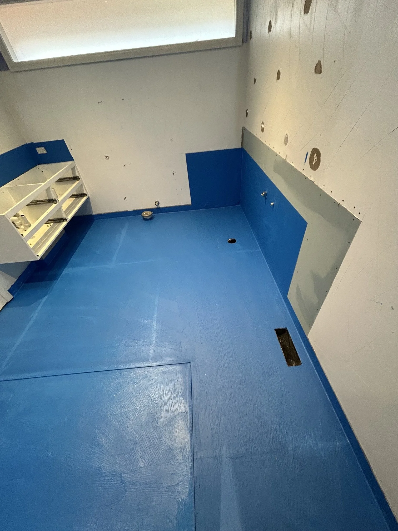 Empty room under construction or renovation with blue and white walls, a built-in shelf, and electrical outlets and holes in the walls and floor.