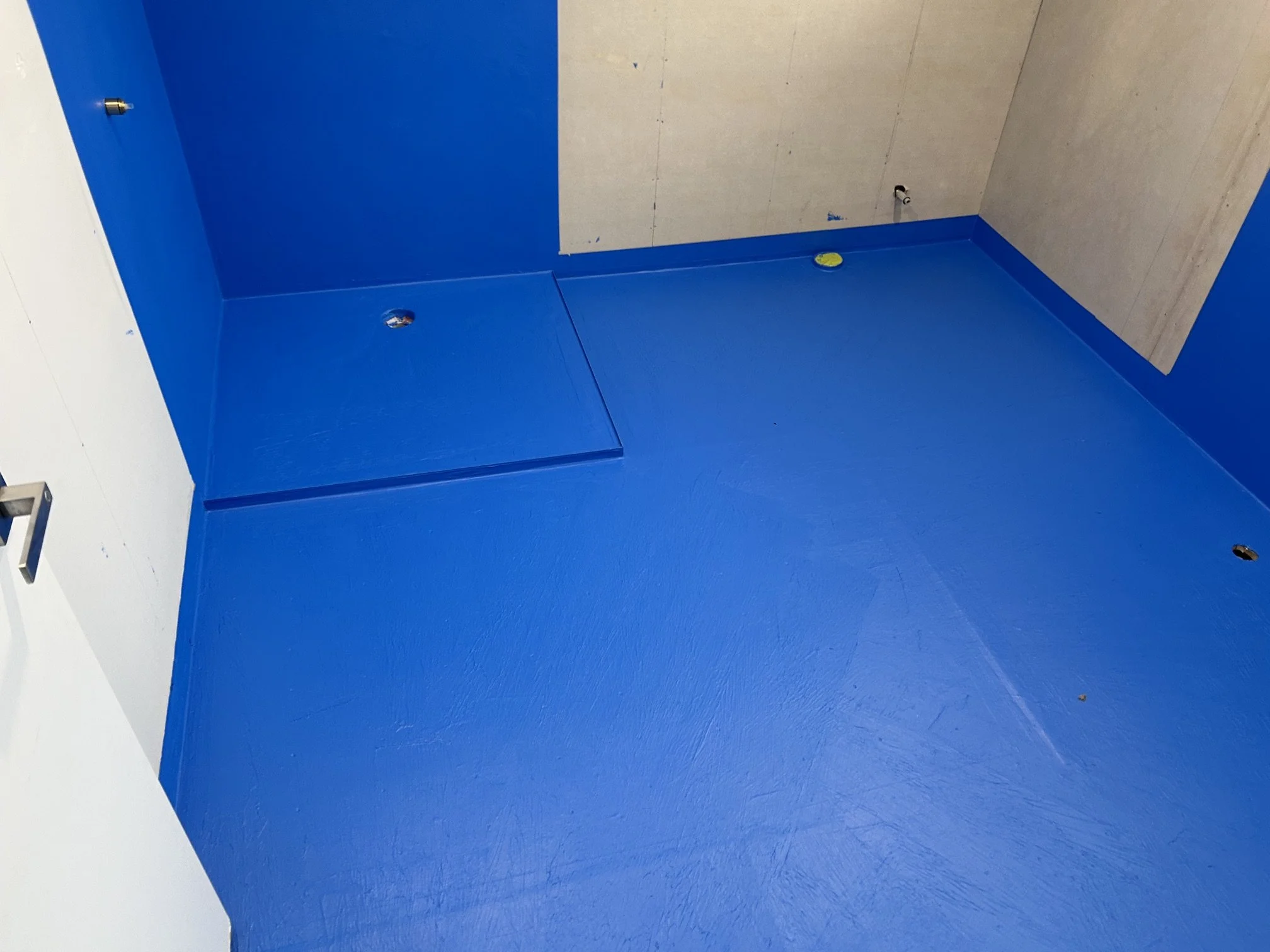 Unfinished blue-tiled shower stall with exposed plumbing fixtures and floor drain