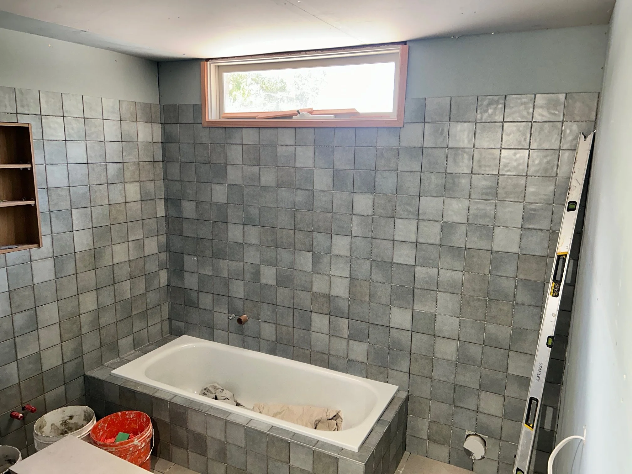 Bathroom under renovation with a white bathtub, gray tiled walls.