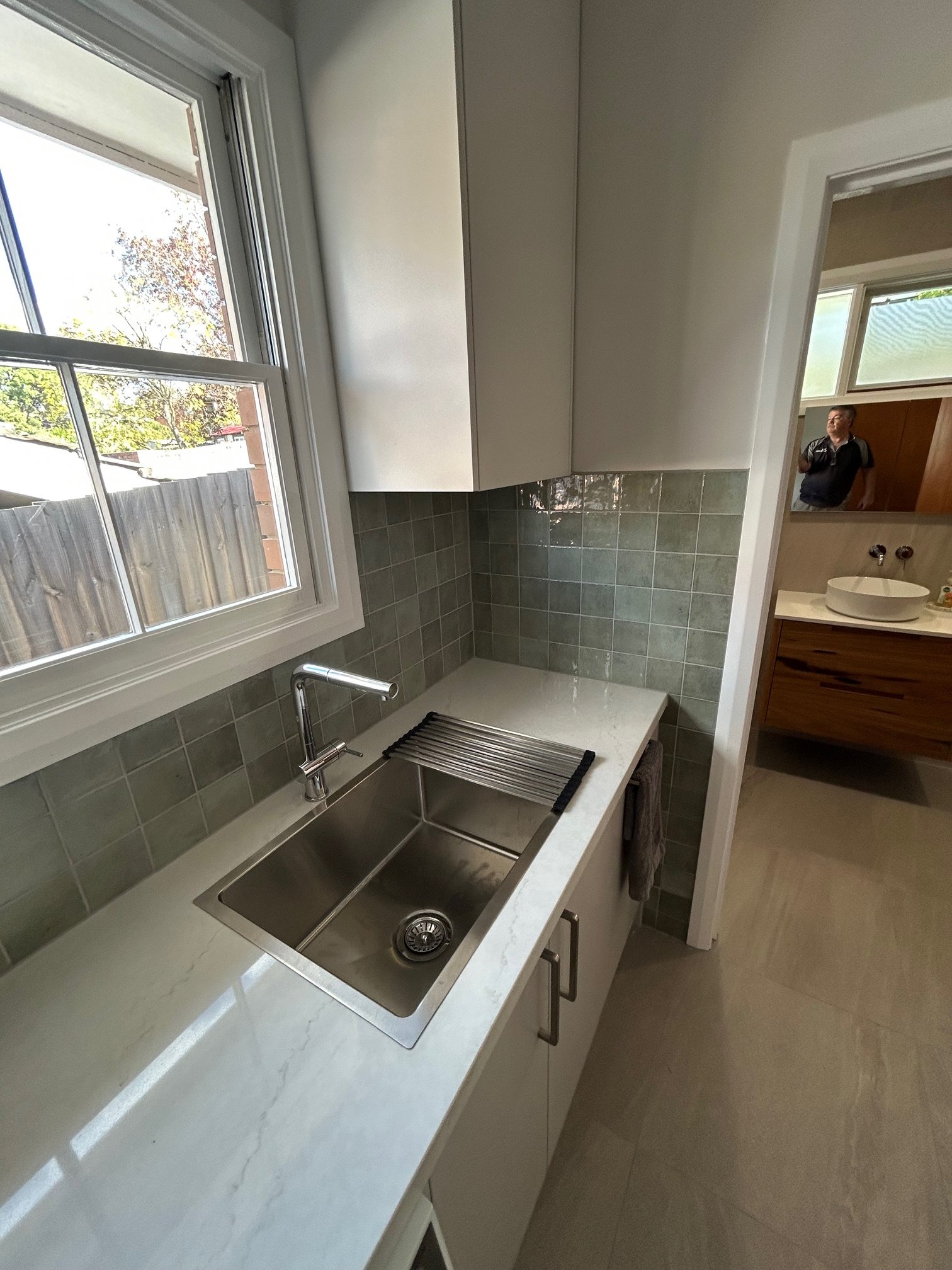 Modern kitchen with a double-basin stainless steel sink, white countertop, gray tile backsplash, white cabinets.