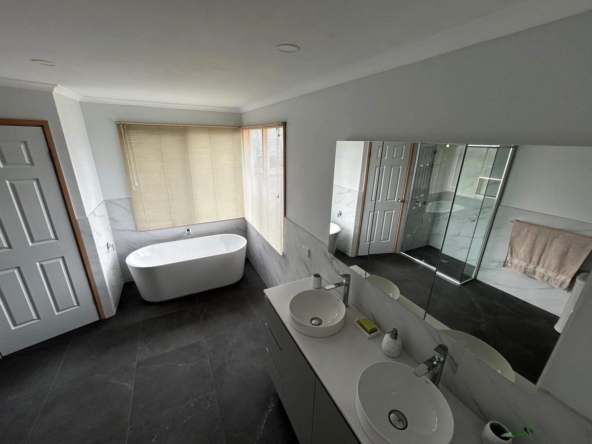 Modern bathroom with freestanding bathtub, double vessel sinks, large mirrored wall, and glass-enclosed shower.