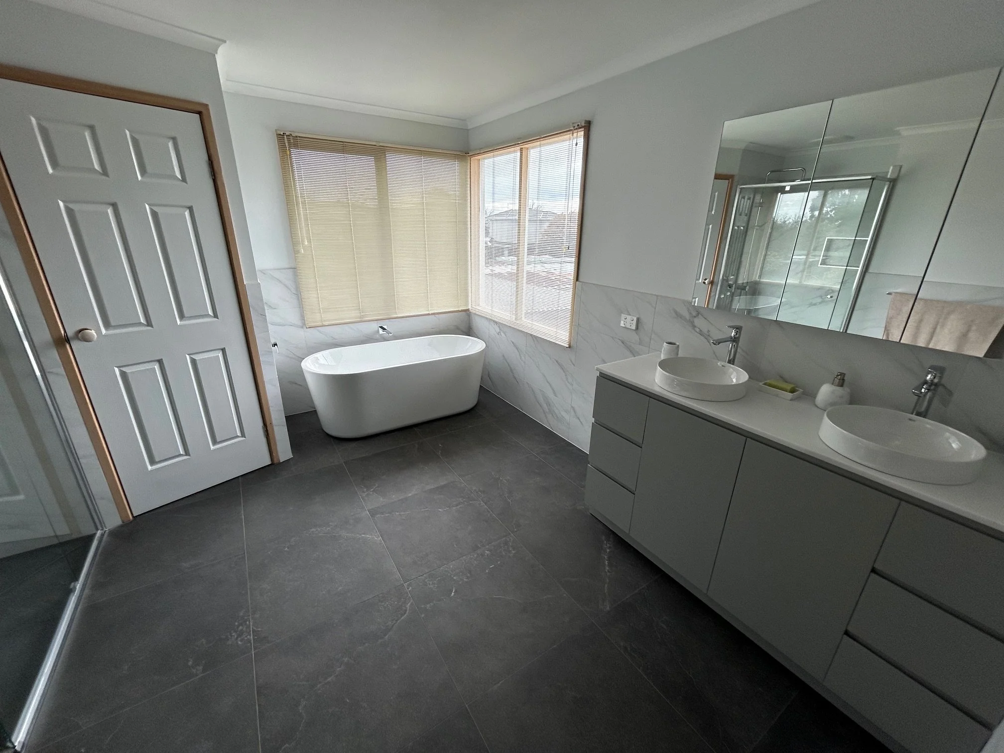 Modern bathroom with a freestanding bathtub, double vessel-sink vanity, large mirror, shower.