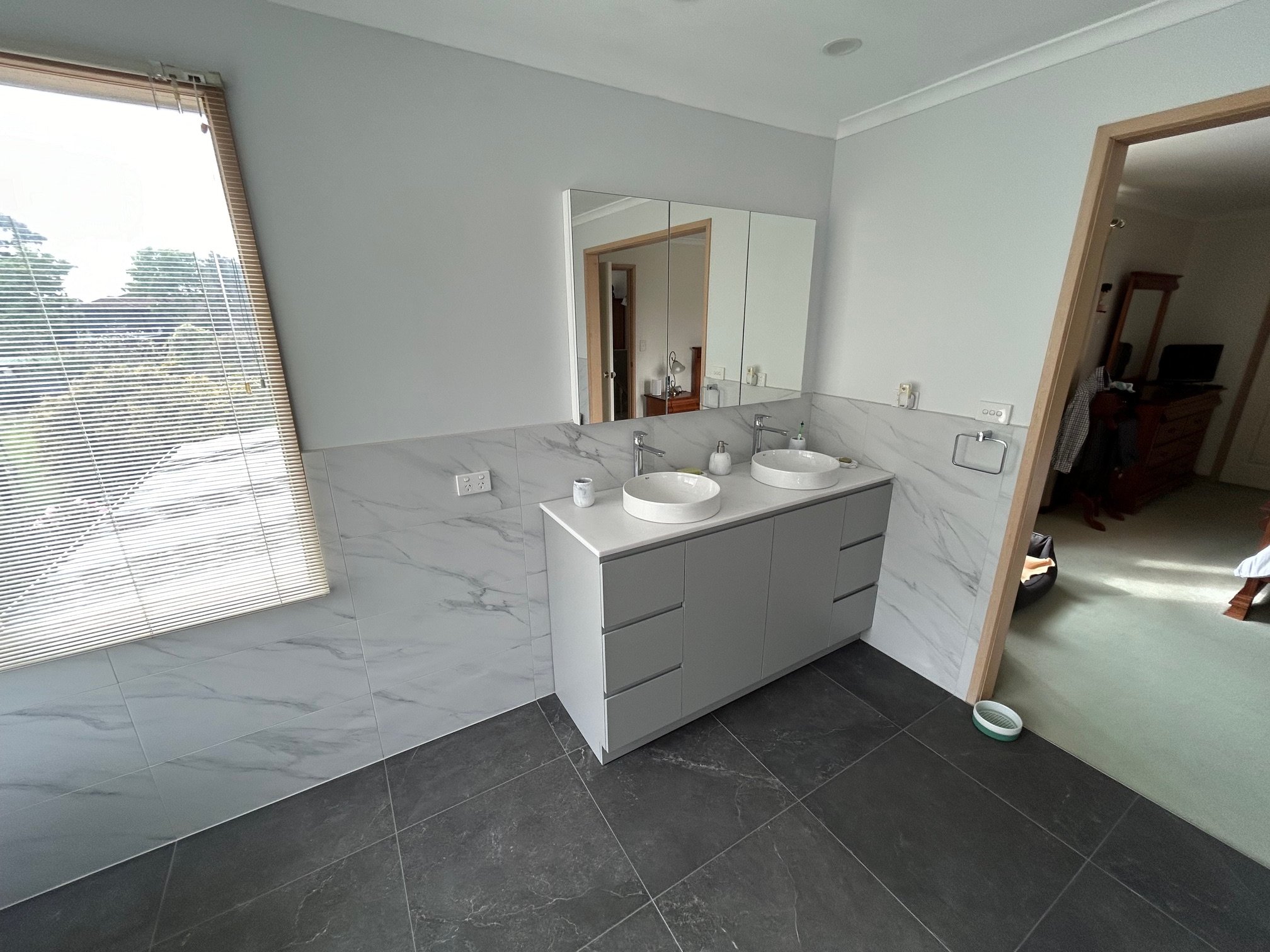 Modern bathroom with double vessel sinks, mirrored vanity, marble-look wall tiles, dark floor tiles.