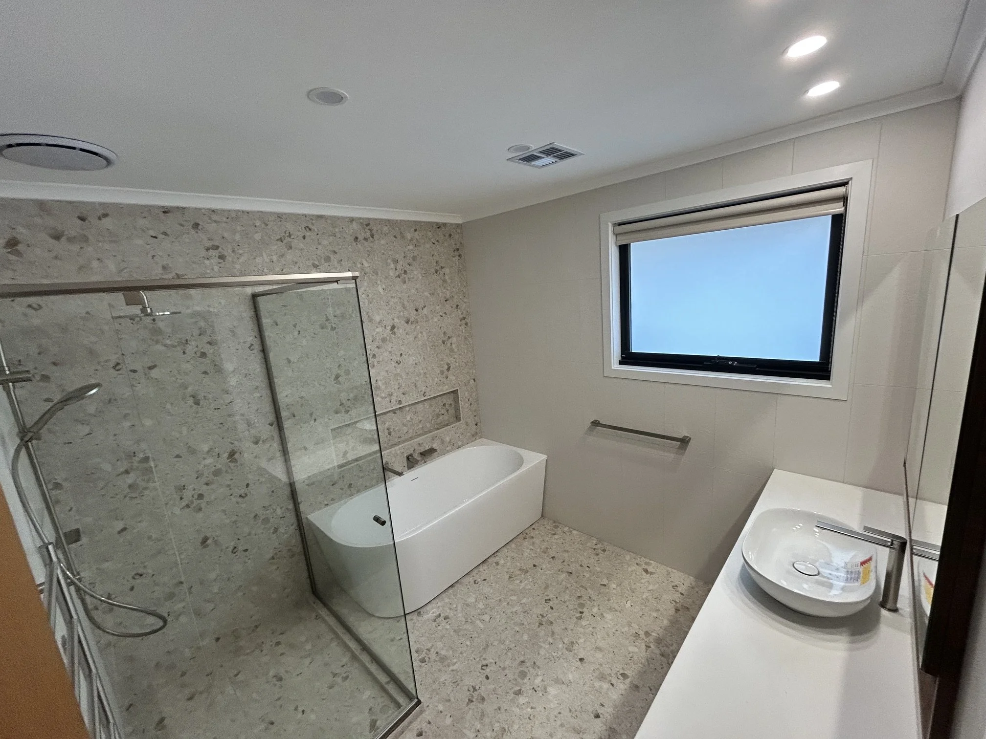 Modern bathroom with a bathtub, walk-in shower with glass door, a window with a blind, and a sink with a soap dispenser.
