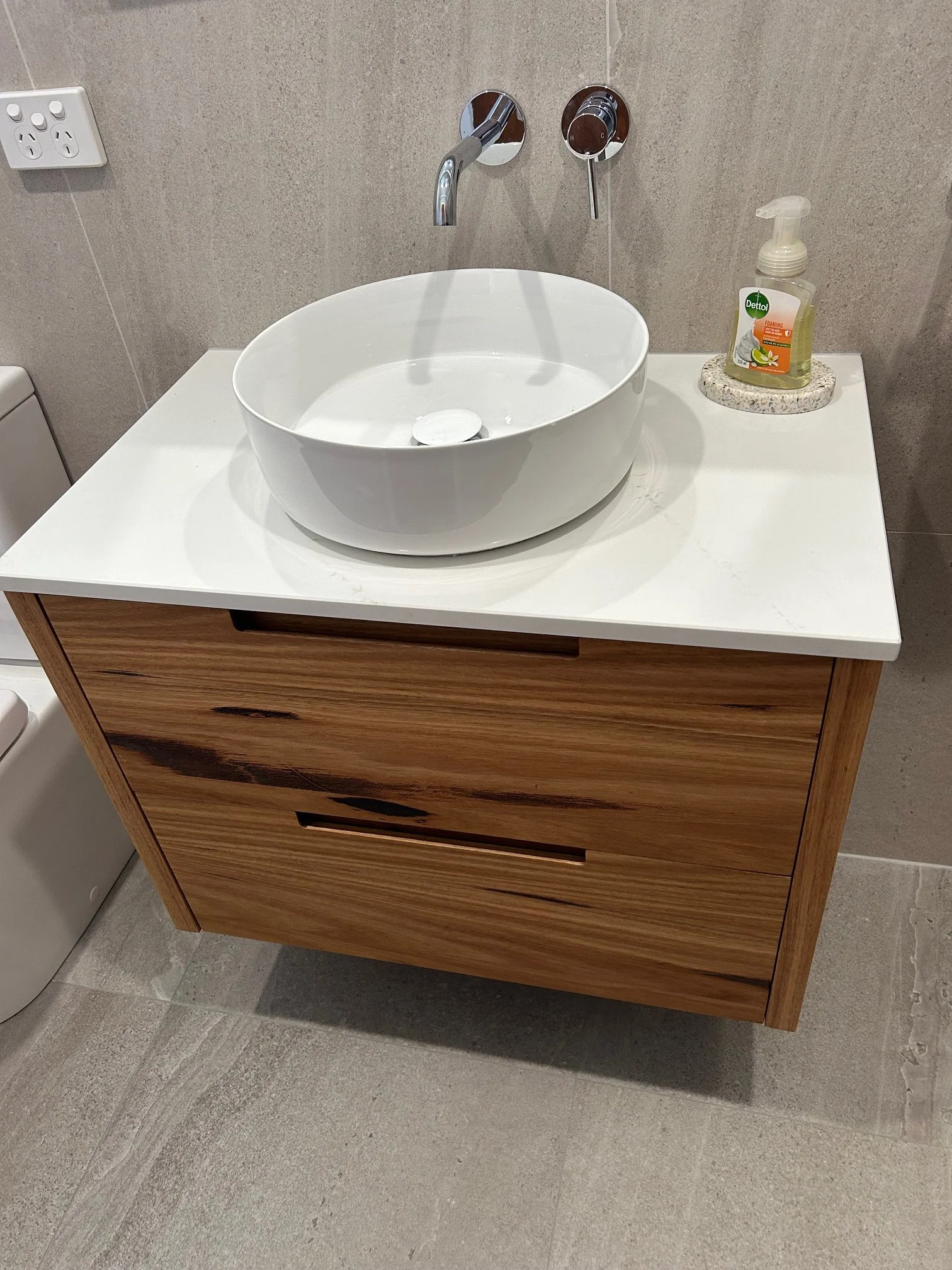 Modern bathroom vanity with white vessel sink, chrome wall-mounted faucet, wooden drawers.