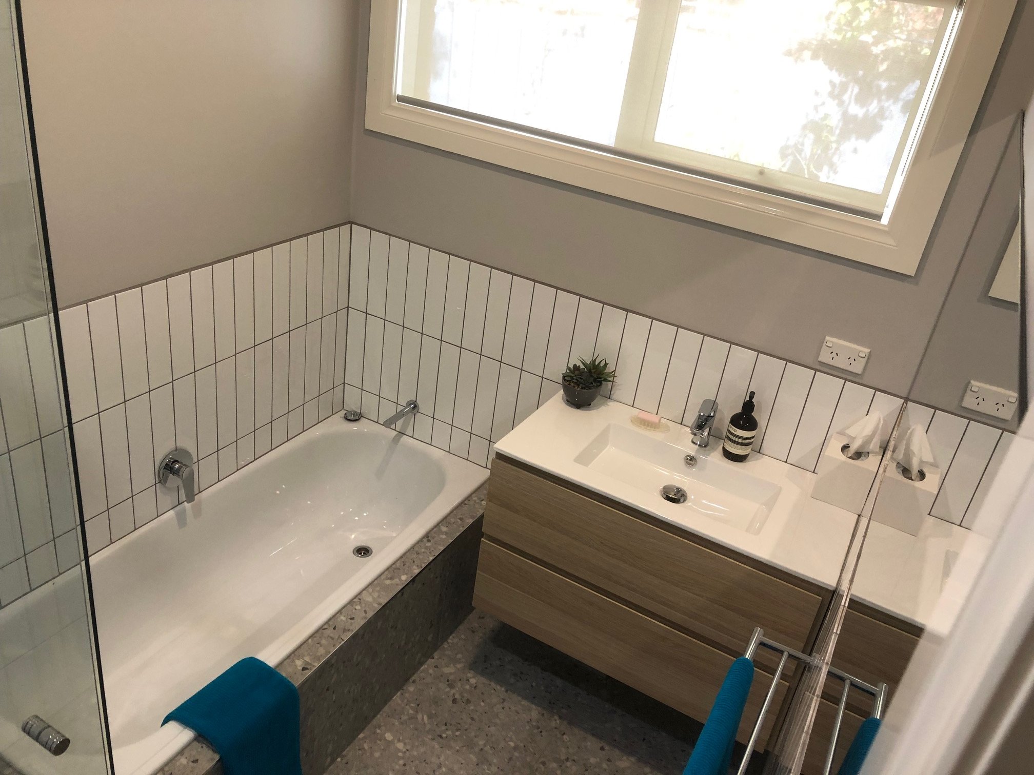Modern bathroom with a white bathtub, wood vanity, rectangular sink, white vertical wall tiles.