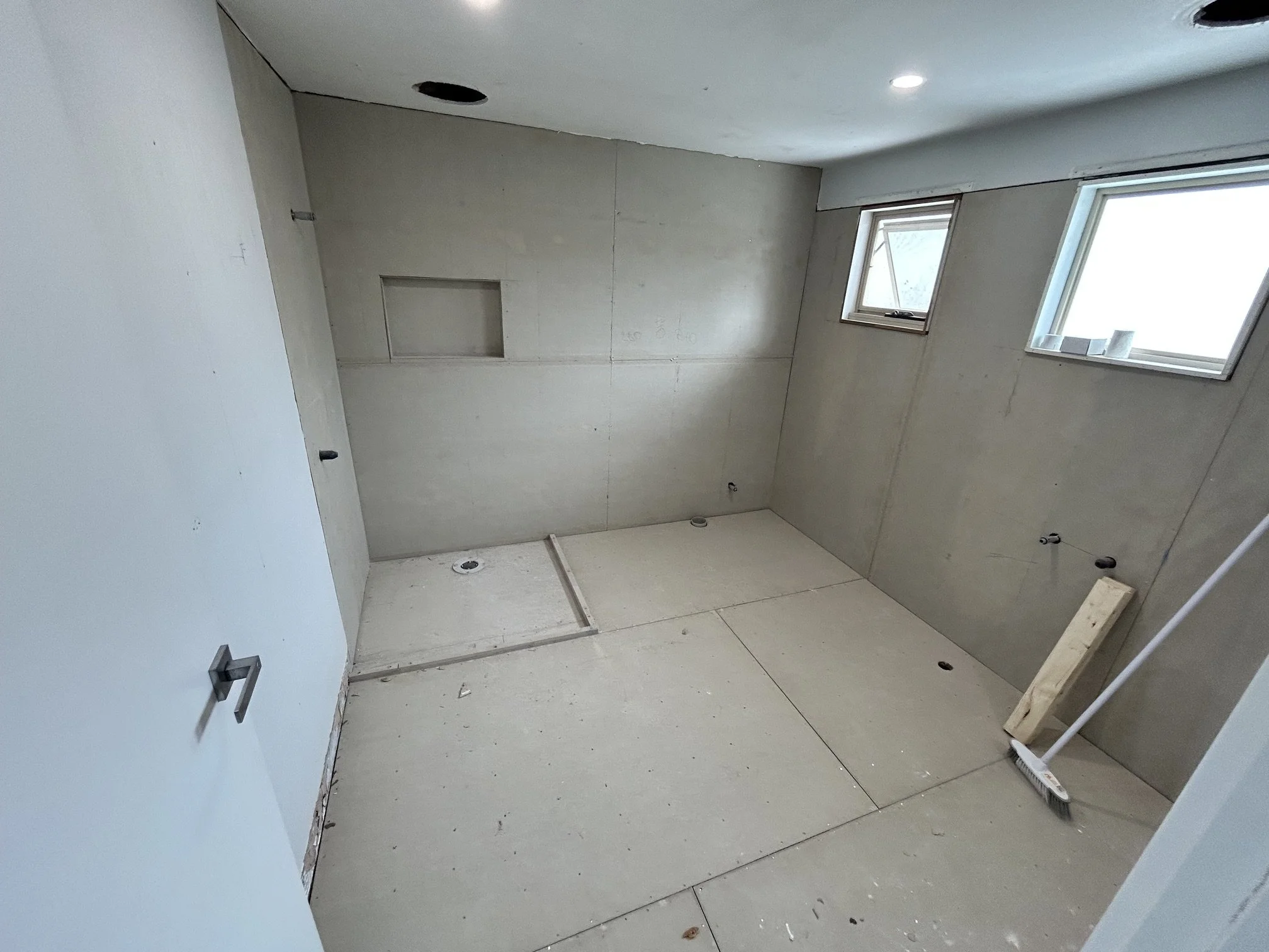 Unfinished bathroom under renovation with cement-board walls, plumbing fixtures, recessed ceiling lights.