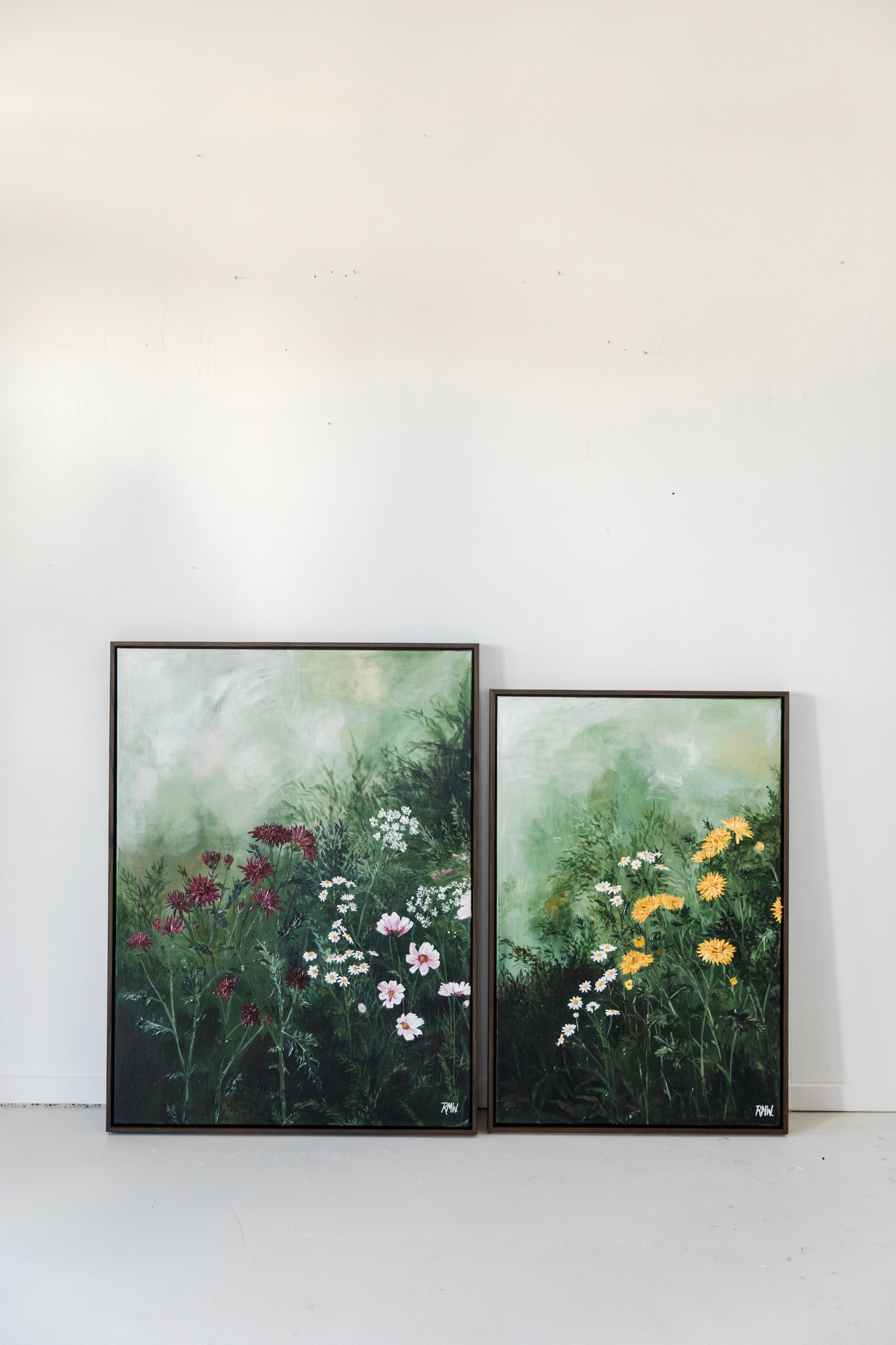 Two framed paintings of wildflowers on a white gallery wall.