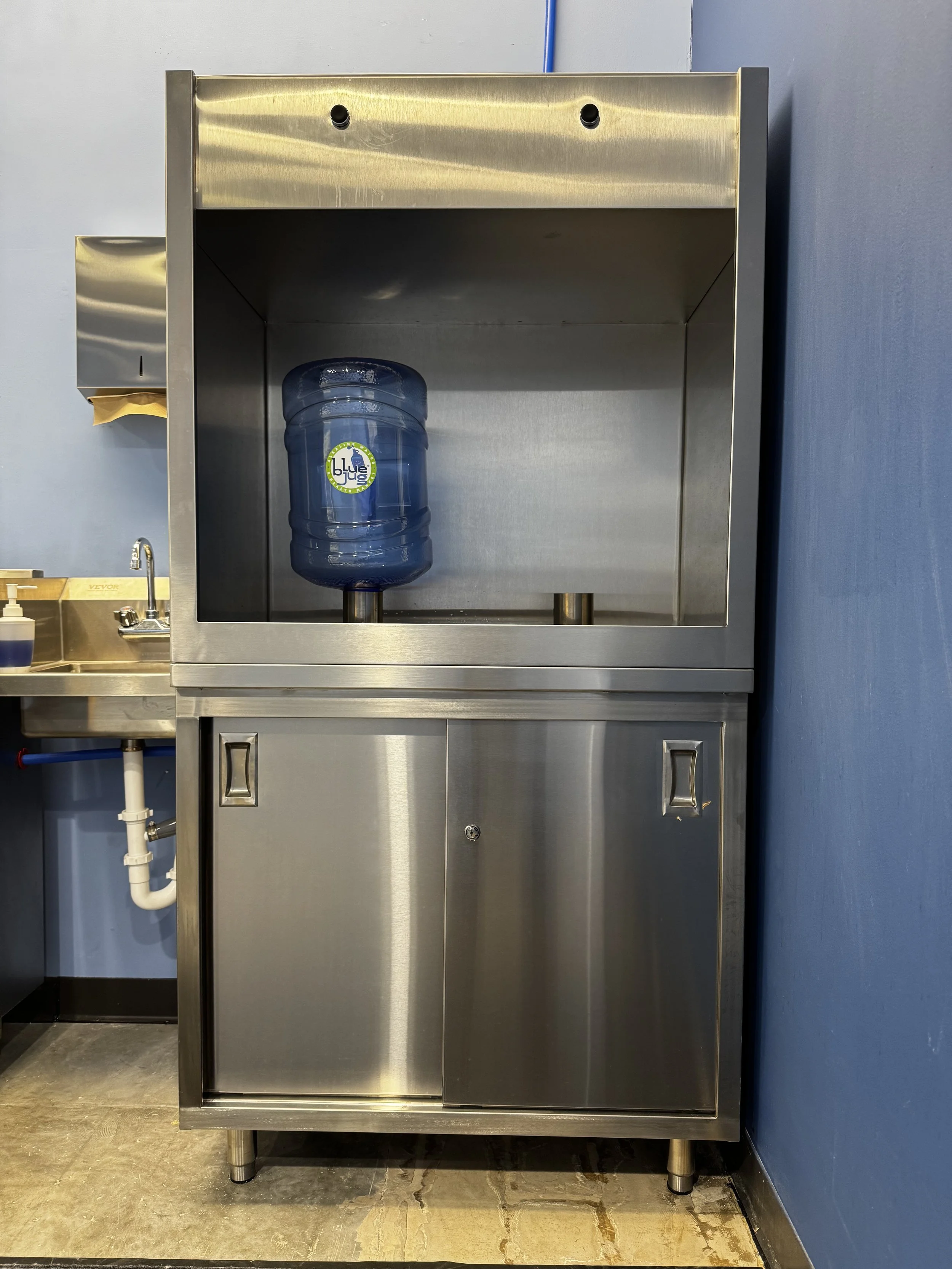 Stainless steel water fountain with a blue water jug and a blue wall in the background.