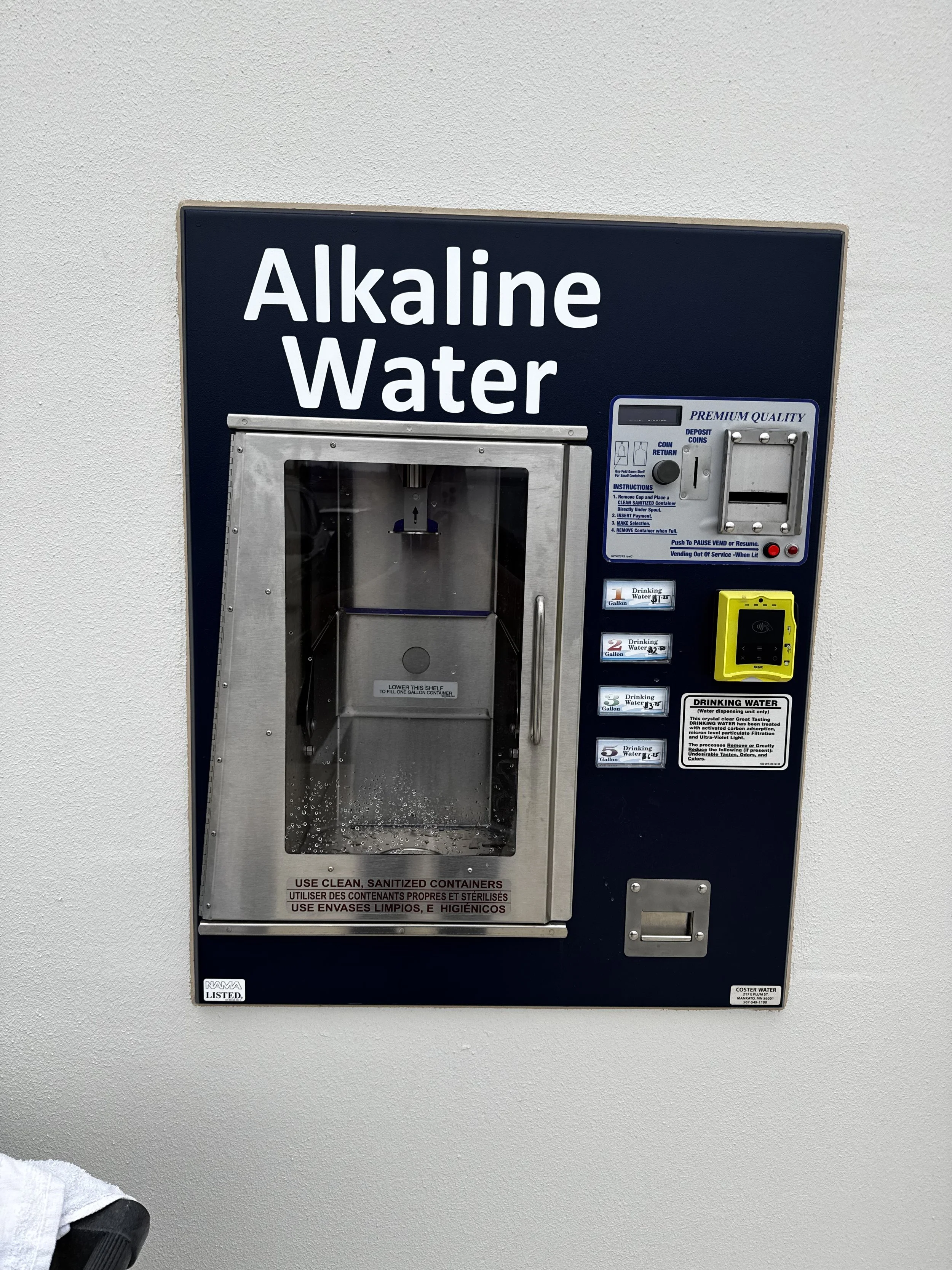 A vending machine for alkaline water mounted on a white wall.
