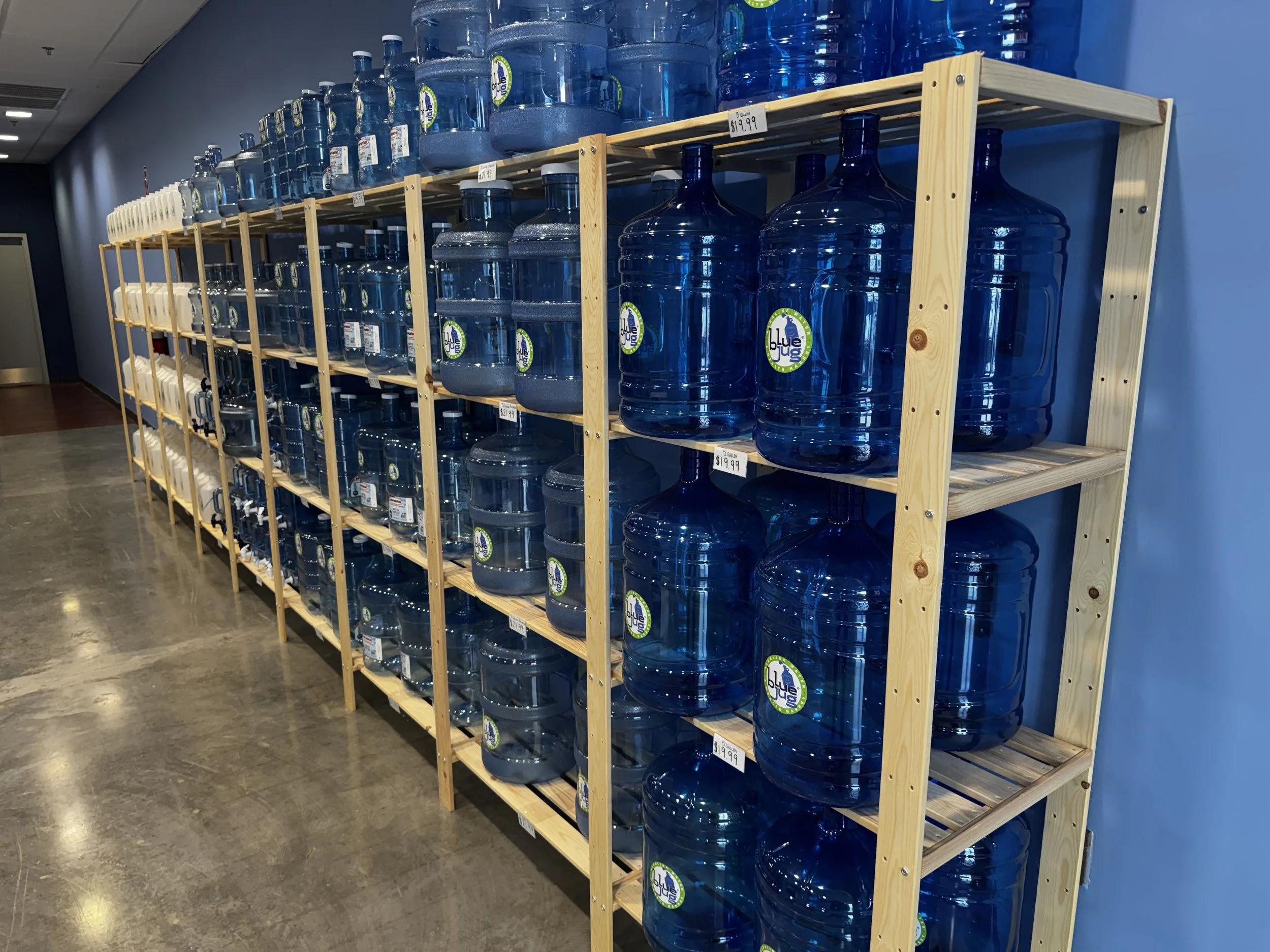 Display of large blue water bottles on wooden shelving in a store.