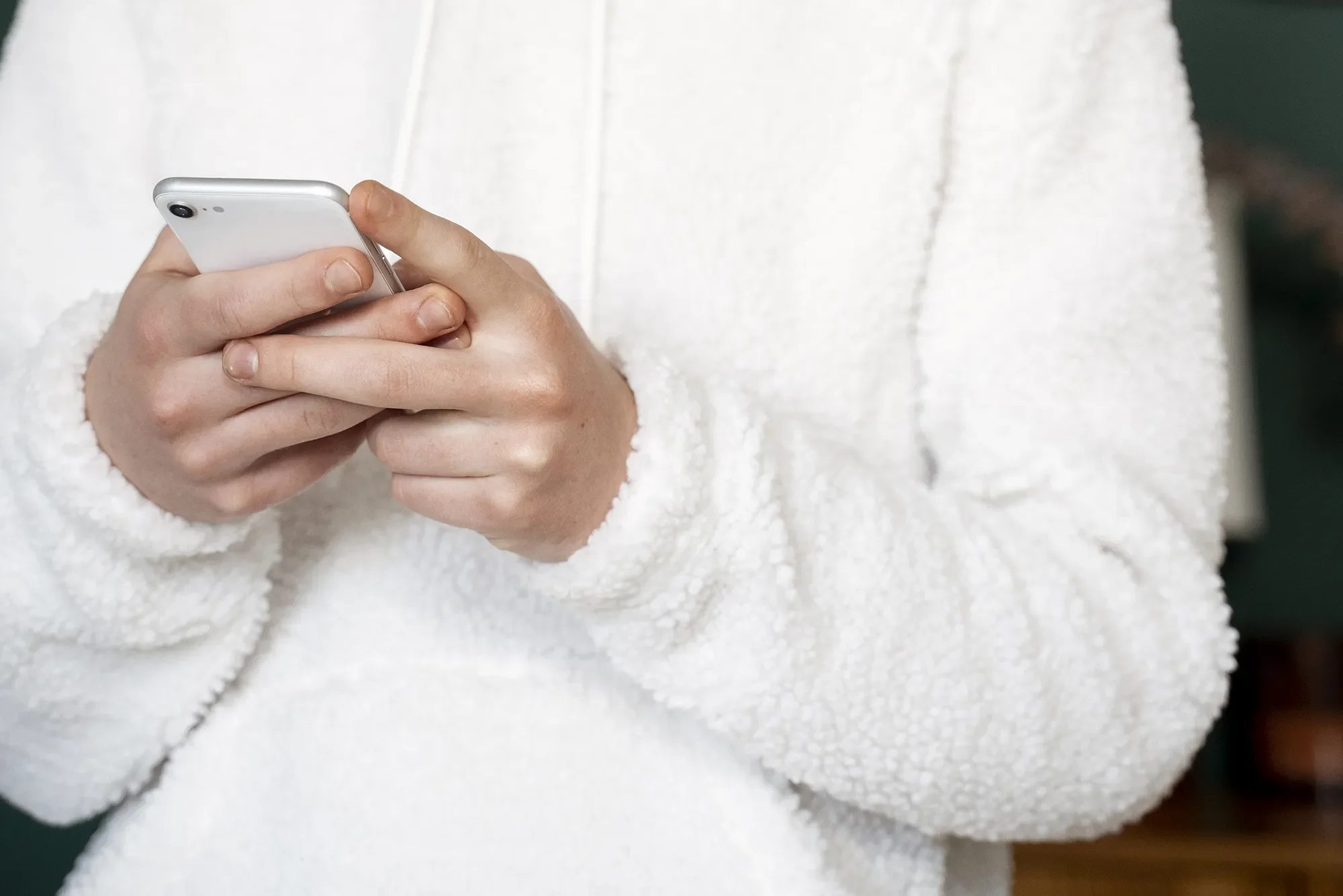 A close-up of hands holding a smartphone, wearing a white fluffy jumper.