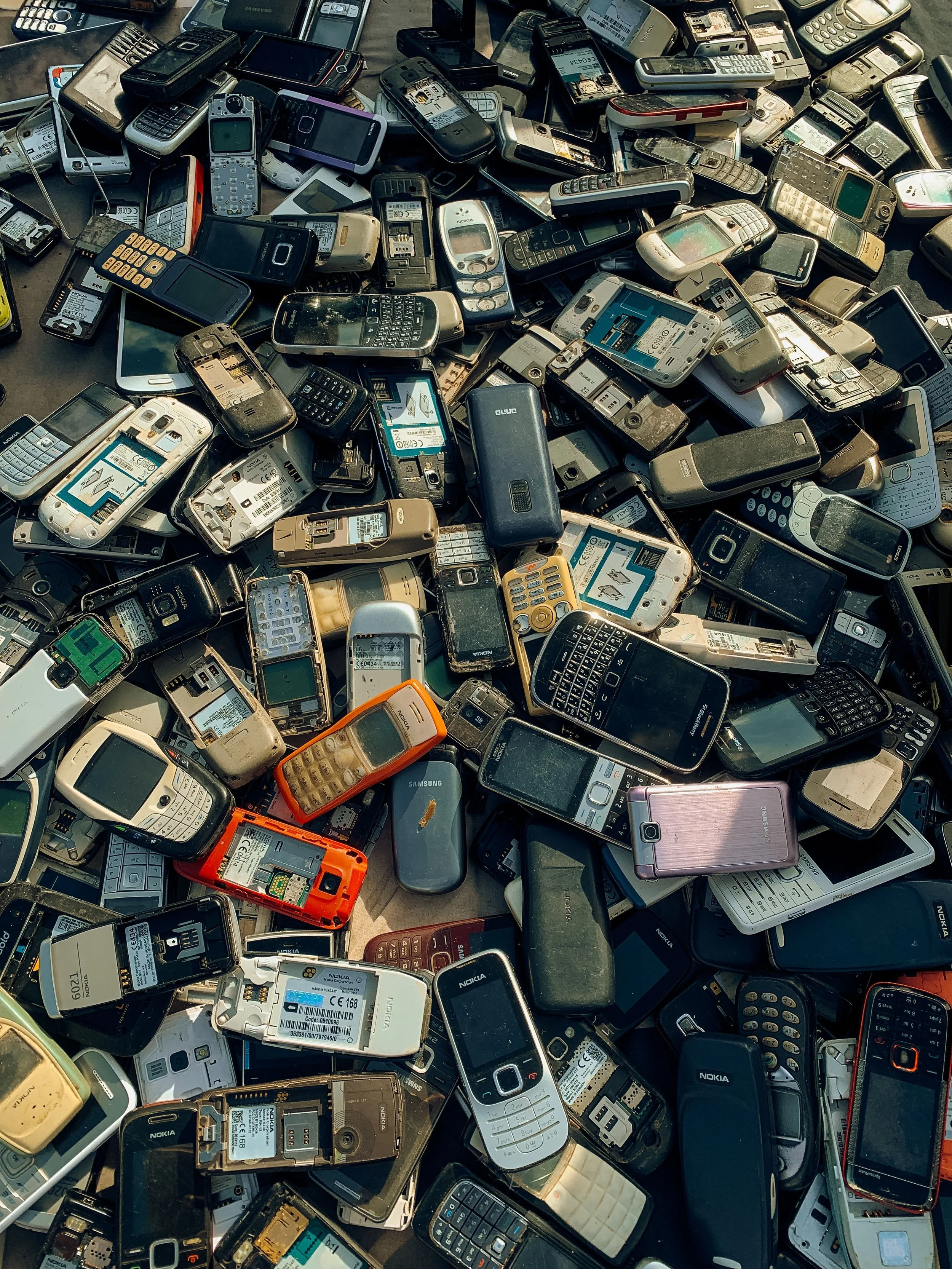 A large pile of old and used mobile phones of various models and brands, including Nokia, Blackberry, and Samsung.