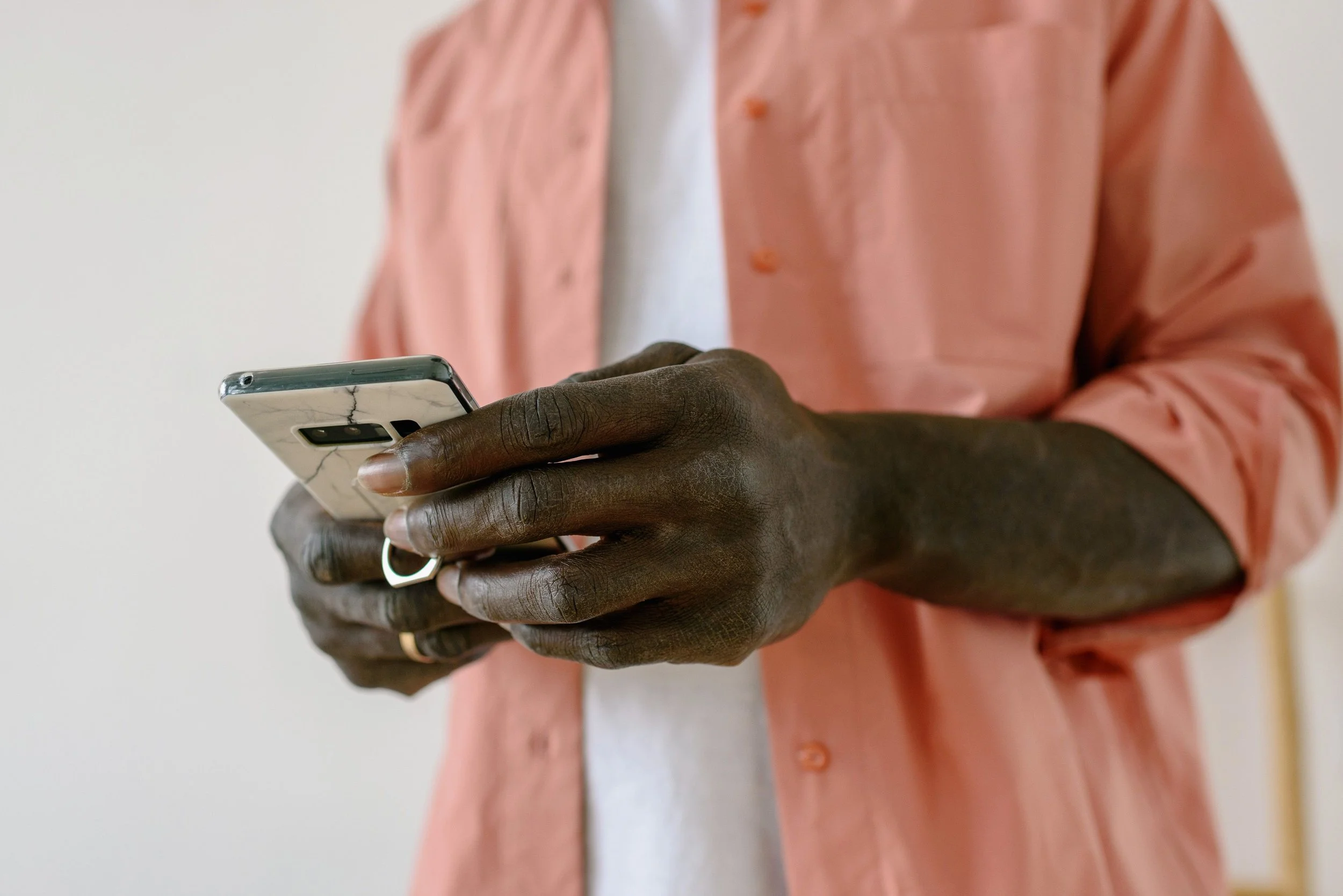 A close-up of hands holding a smartphone with a marble-effect case, wearing a pink shirt.