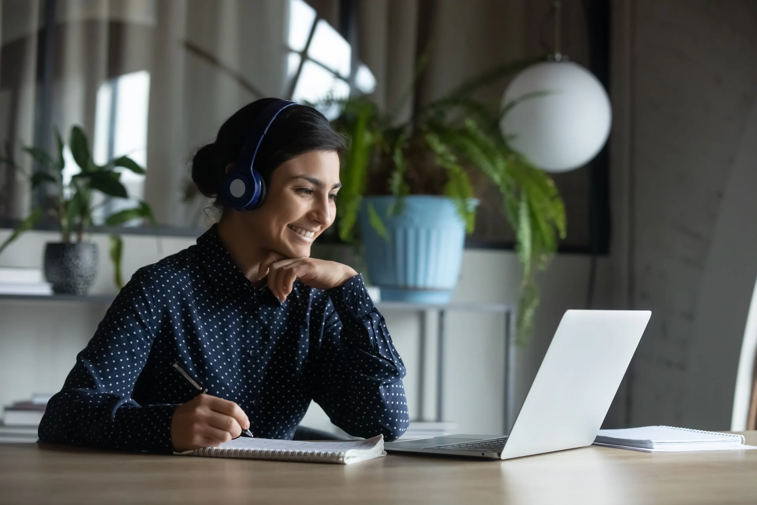 woman engaging in a video call while taking notes on a laptop at her desk.