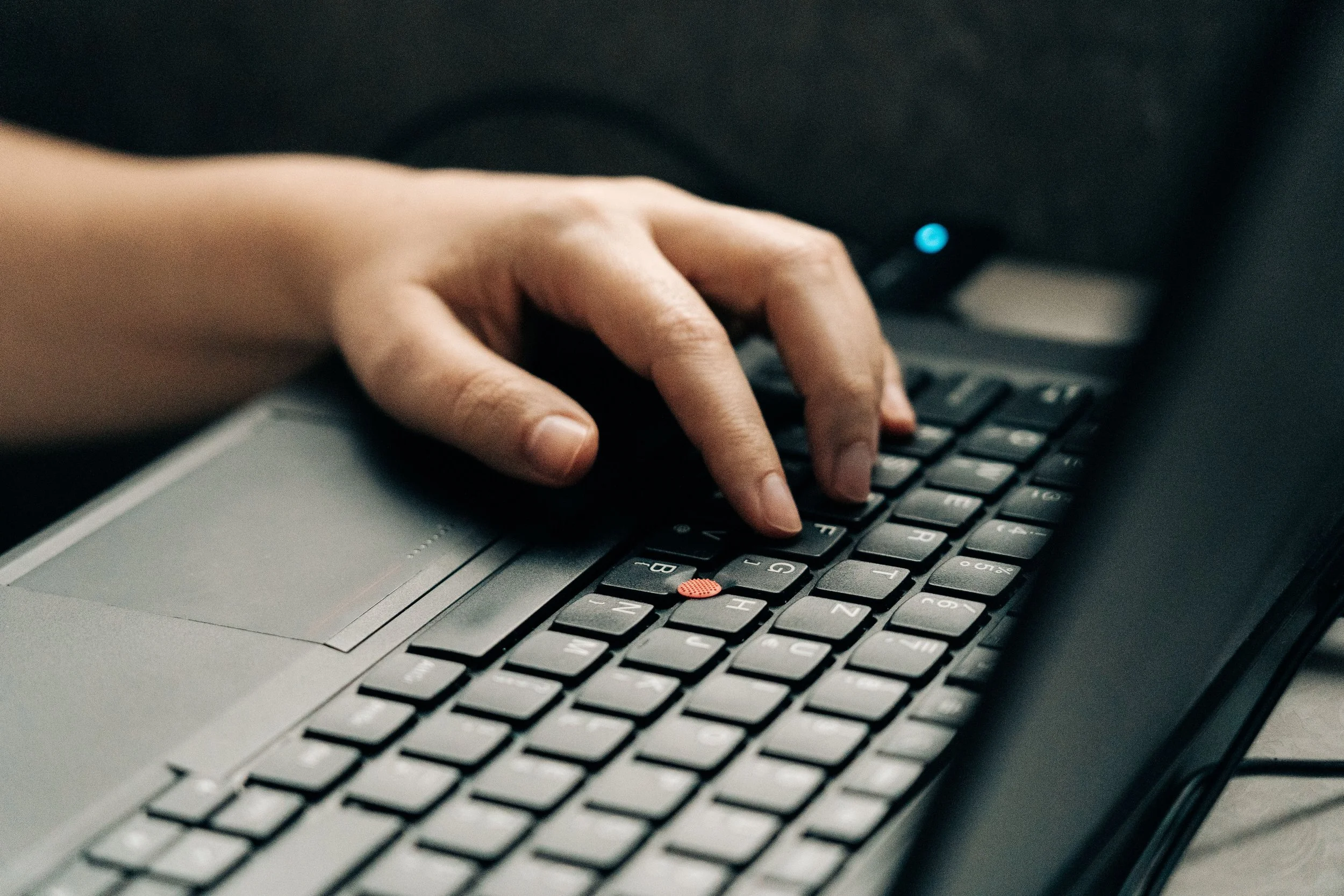 Close-up of a person's hand typing on a laptop keyboard with a black background.