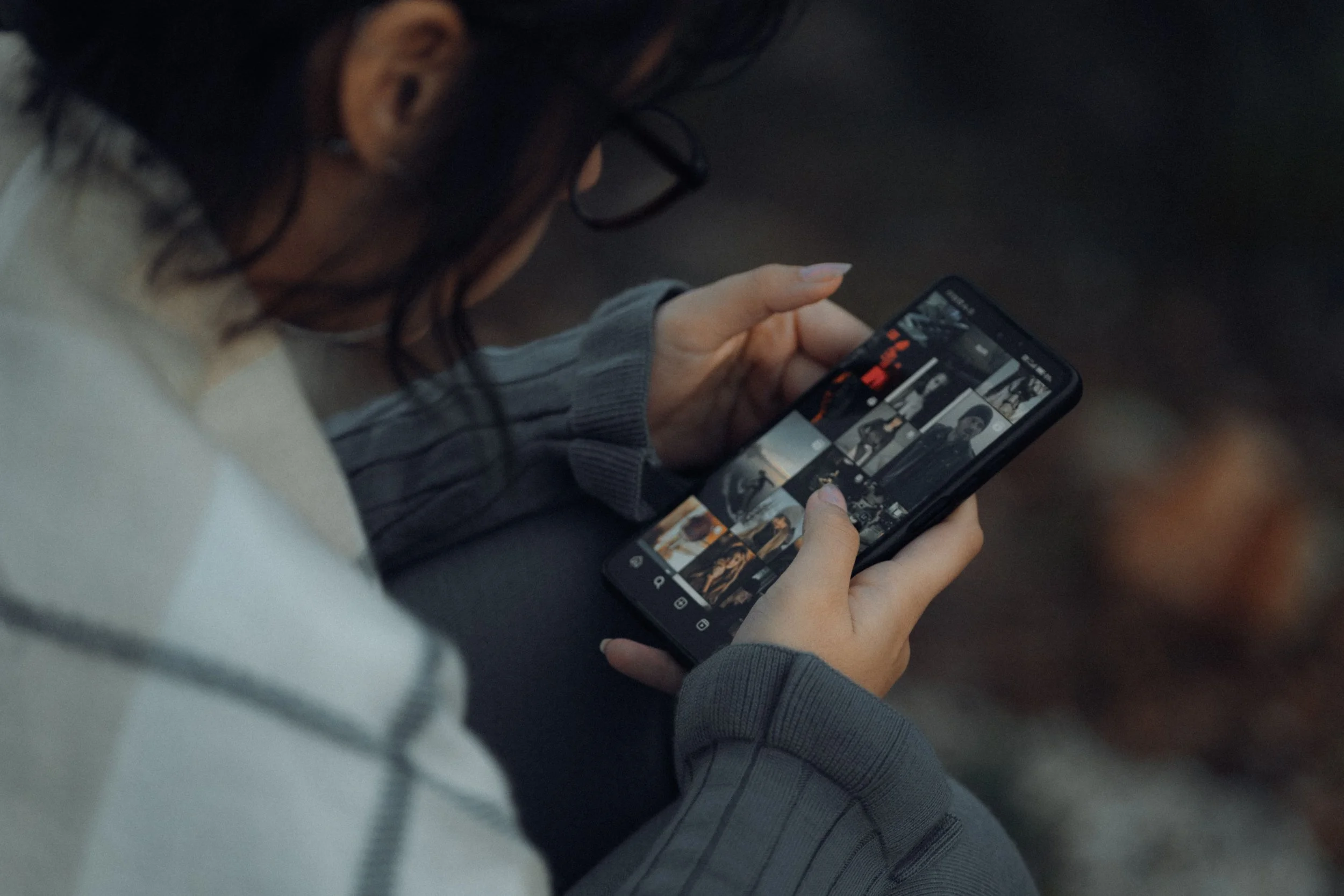 A woman with glasses scrolls through Instagram on her phone outdoors.