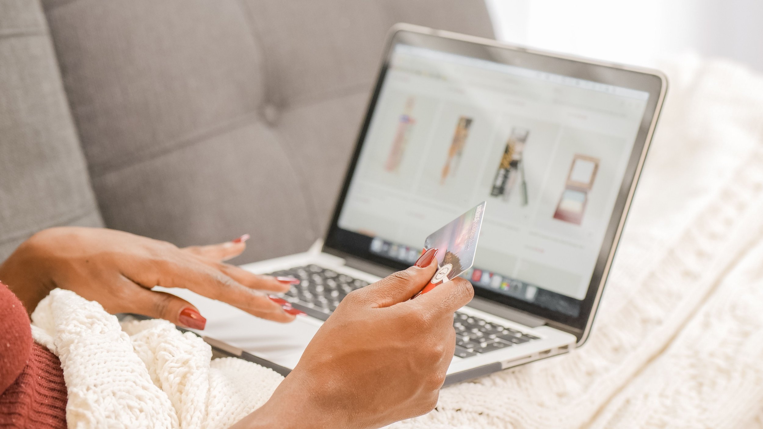 A person holds a bank card while typing on a laptop showing a beauty product shopping website.
