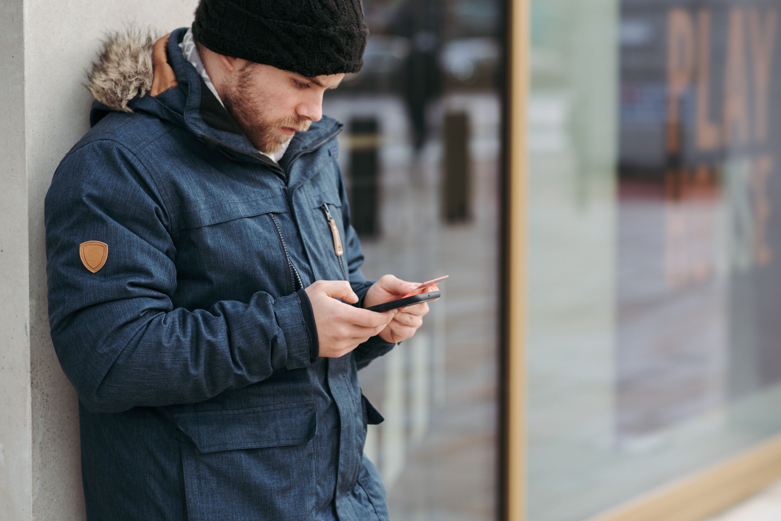 A man in a coat checks his phone while standing outdoors.