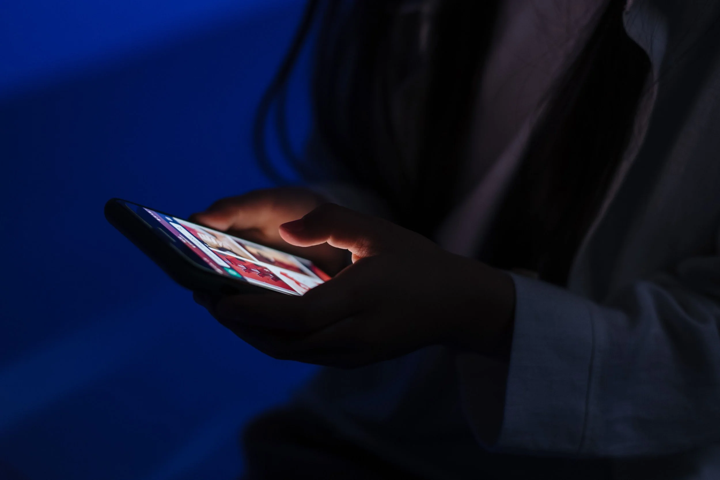 Image 2: A close-up of a hand scrolling through a glowing phone screen in the dark.