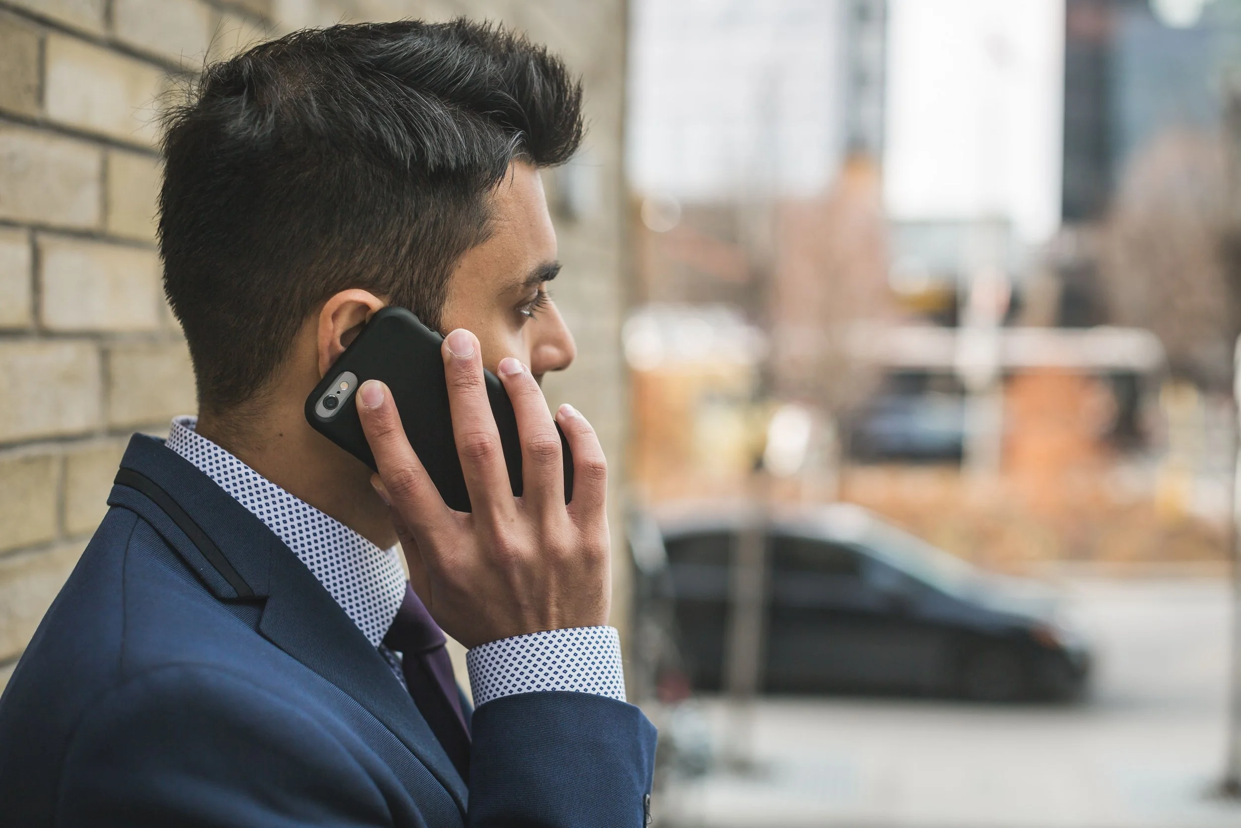 A man in a suit and tie is talking on his phone outdoors.