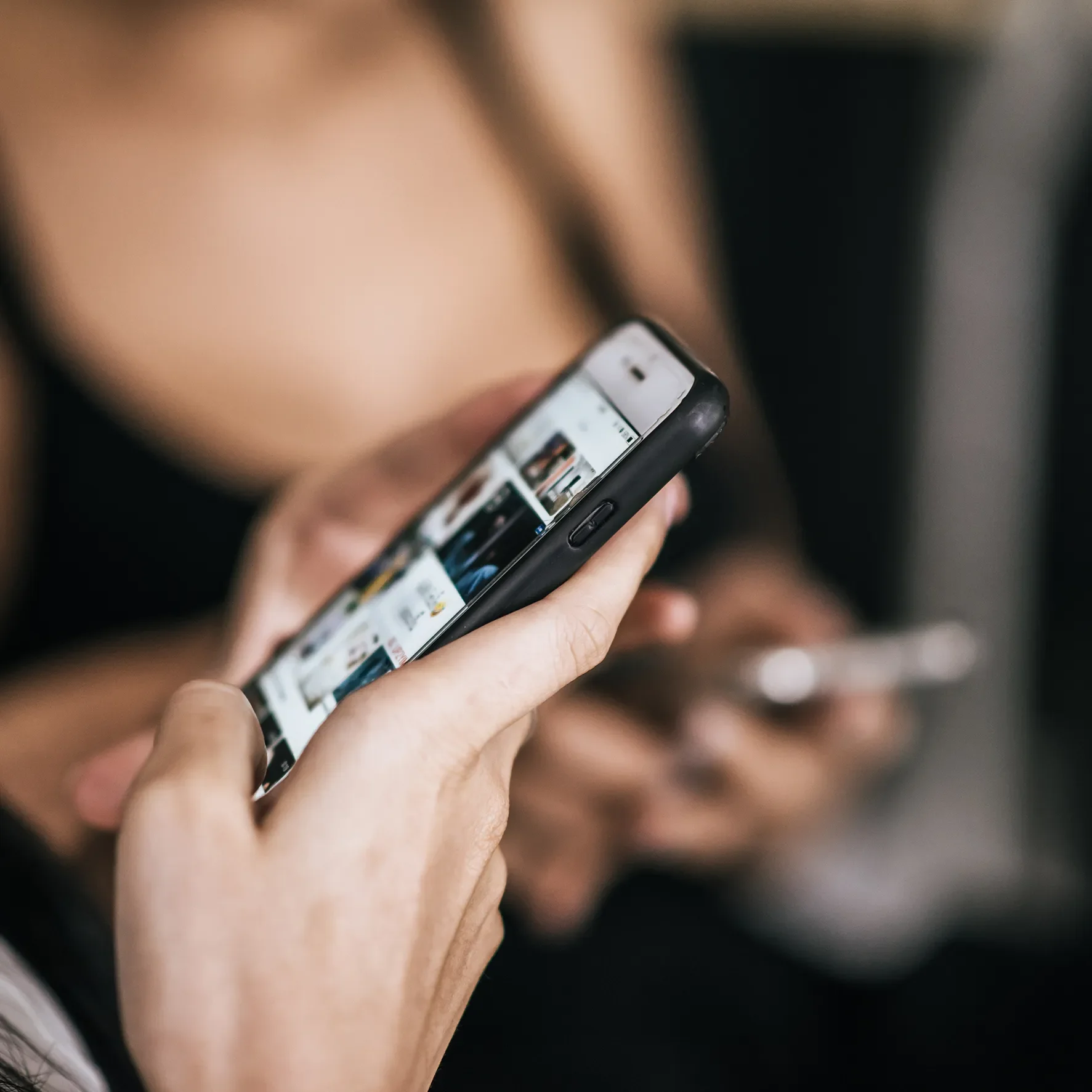 Close-up of a person's hand holding a smartphone, viewed at an angle, with a blurred background.