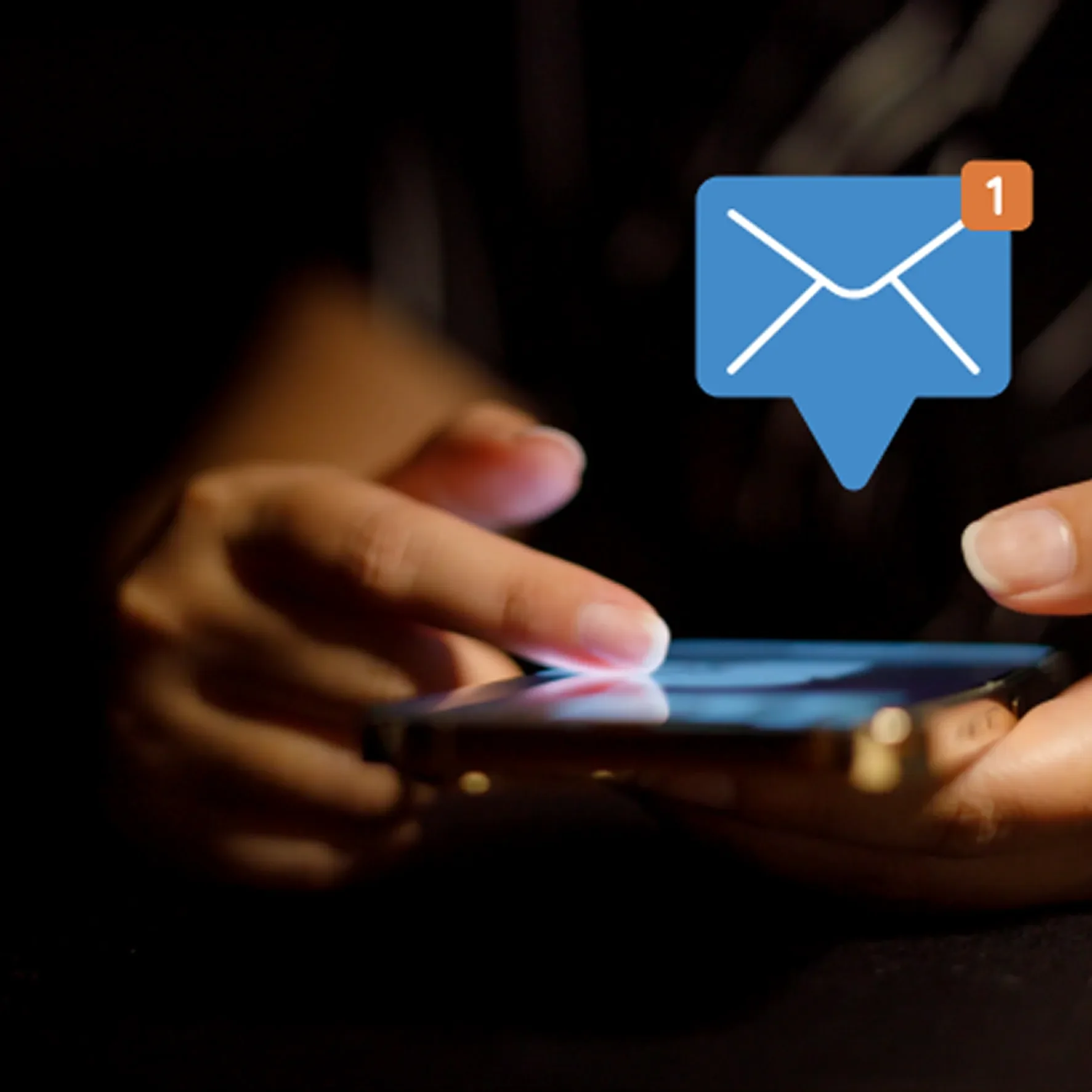 Close-up of a person's hands holding a smartphone in a dark environment, with a notification icon for one new email or message visible on the screen.