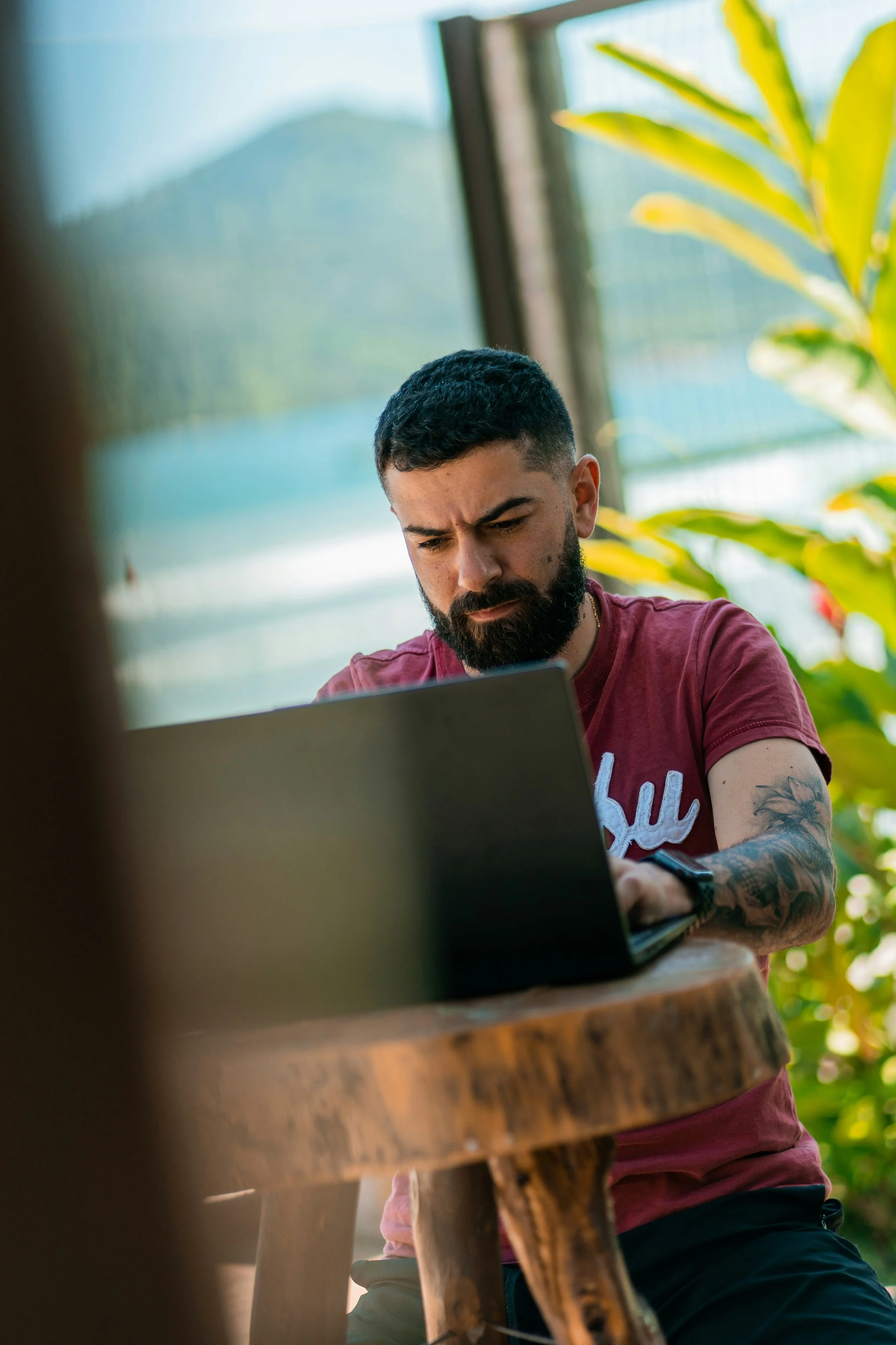 A bearded man with tattoos concentrates on a laptop.
