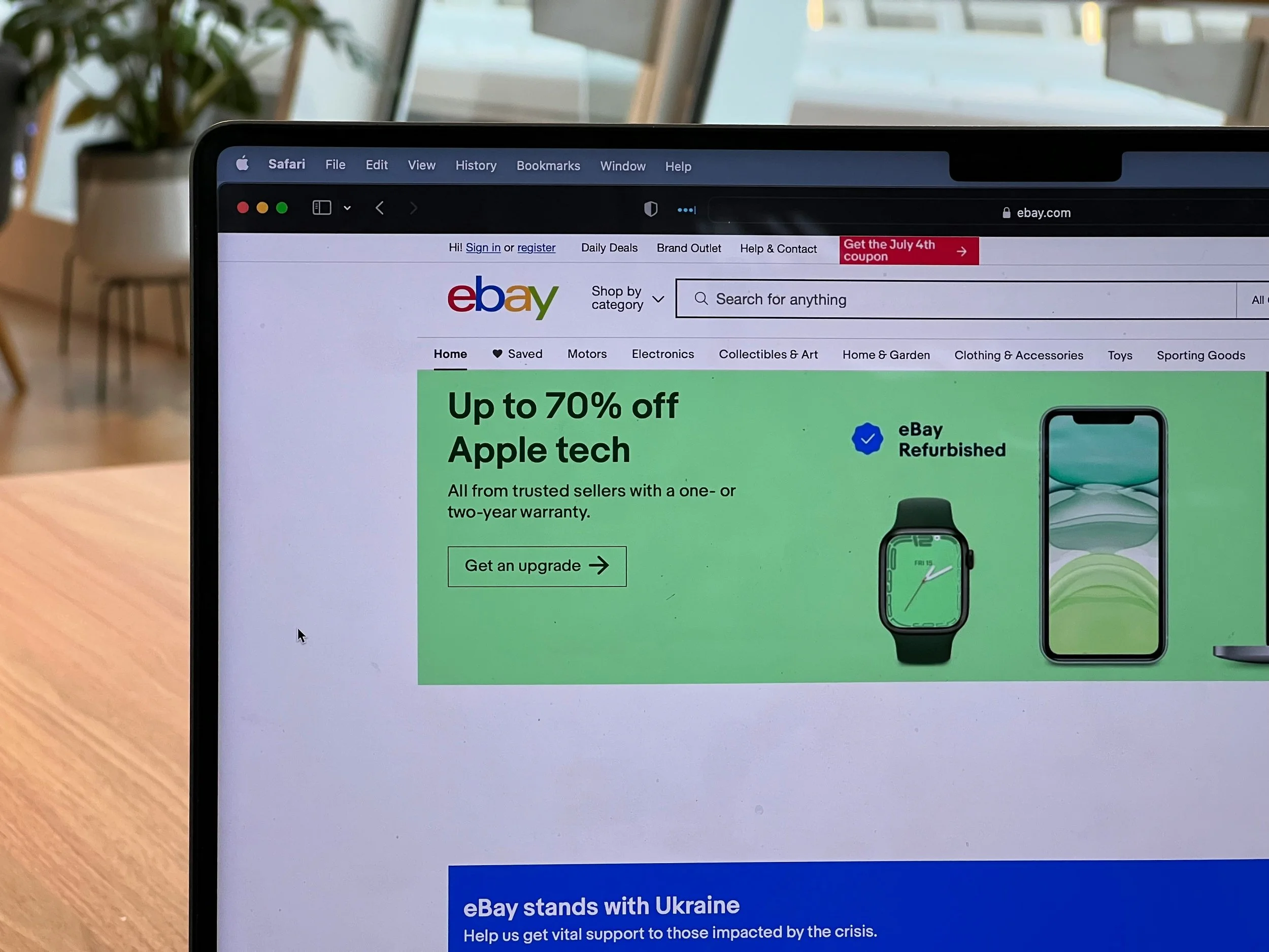 A laptop screen showing the eBay homepage with a promotional banner advertising up to 70% off refurbished Apple tech.