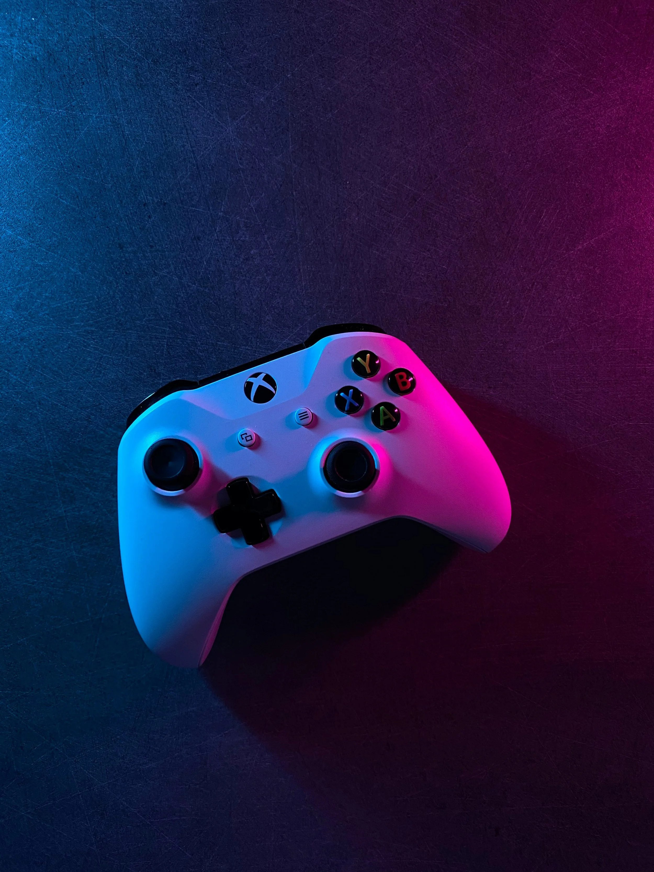 A white Xbox controller lit by blue and pink neon light against a dark background.