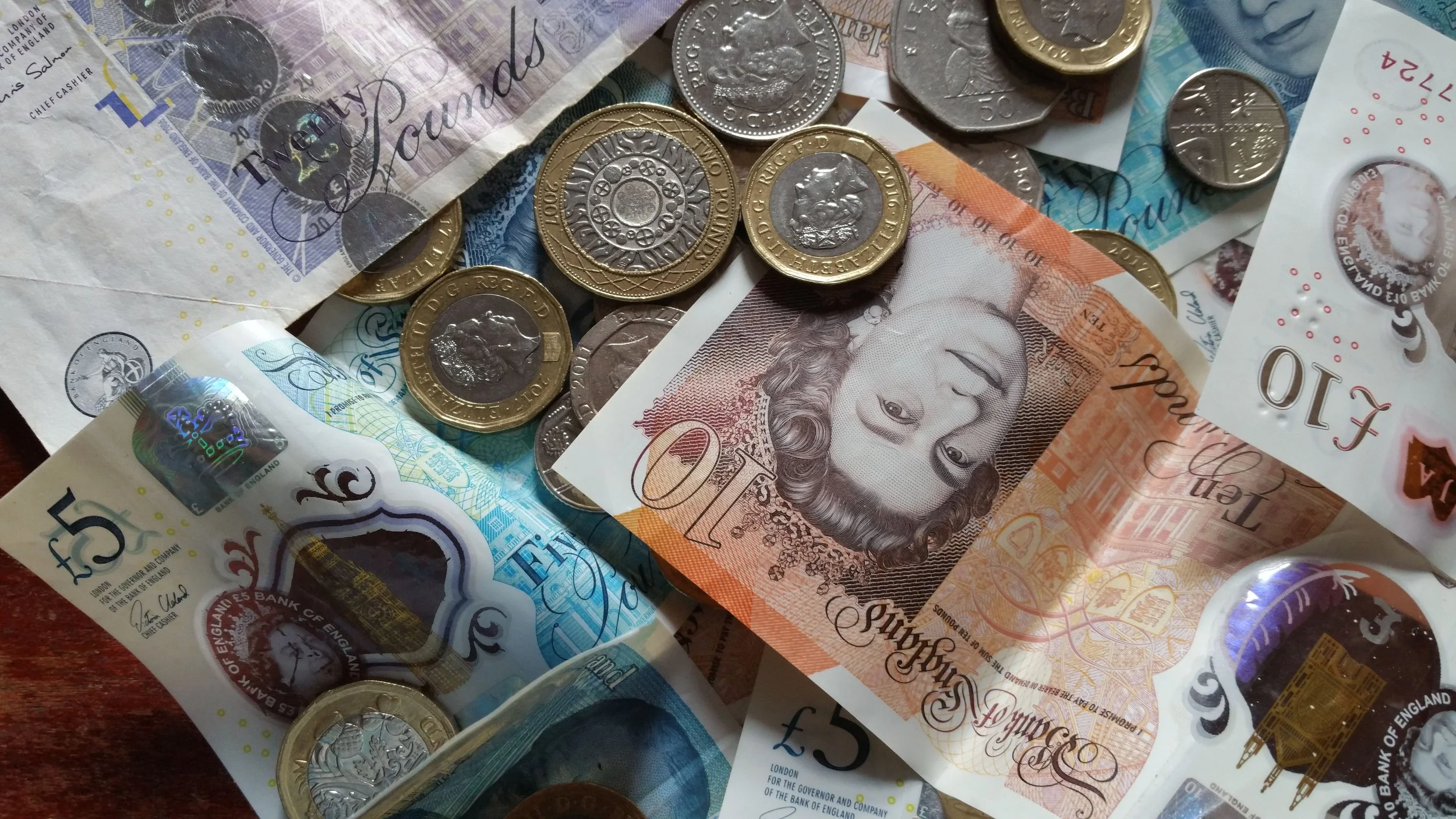 A pile of British currency notes and coins stacked on a wooden table.