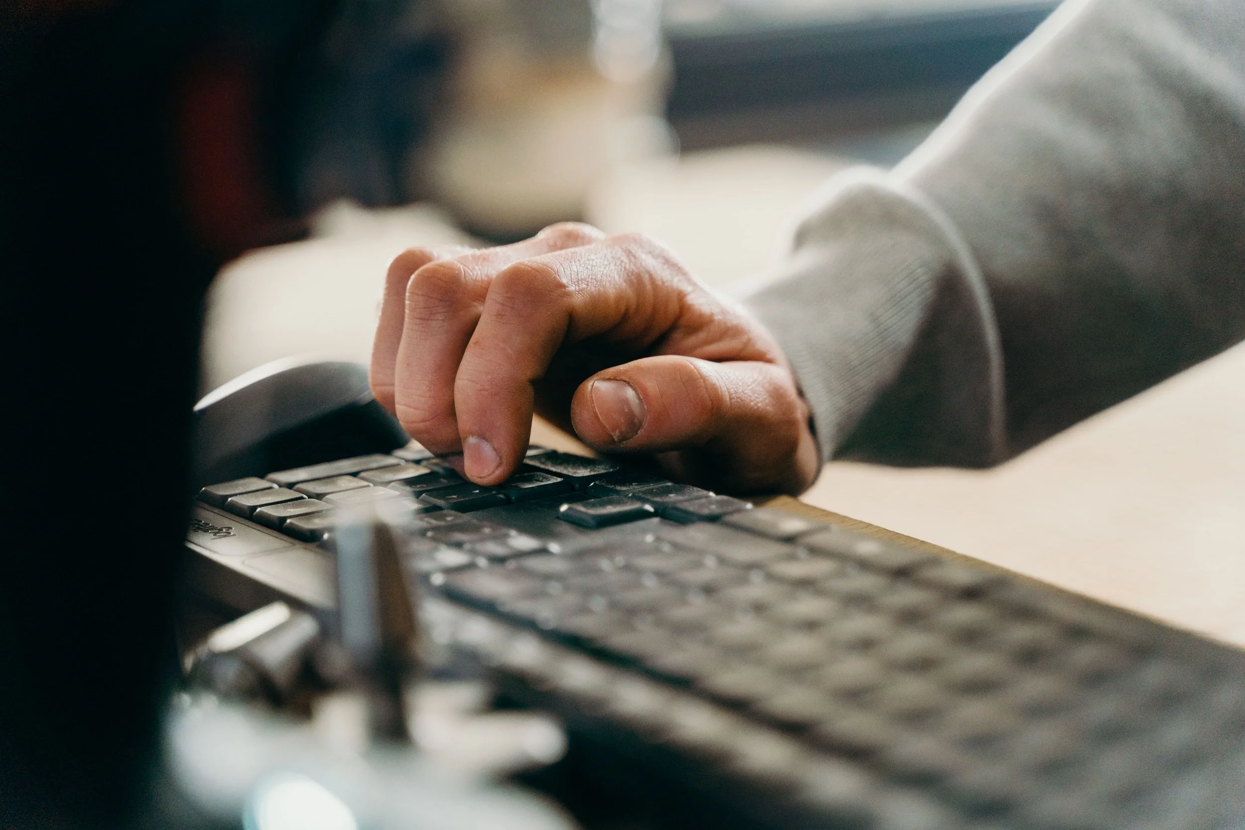 A close-up of a hand typing on a dark keyboard, wearing a grey long-sleeved top.