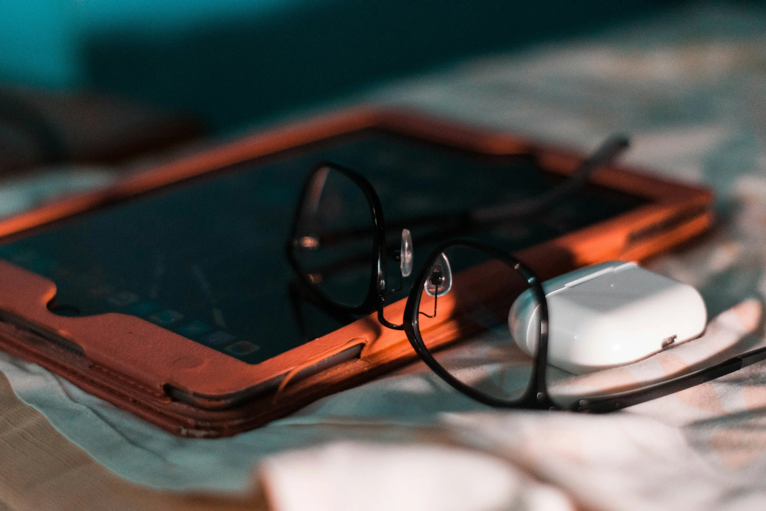 A tablet in an orange case, a pair of glasses, and wireless earbuds resting on a surface.