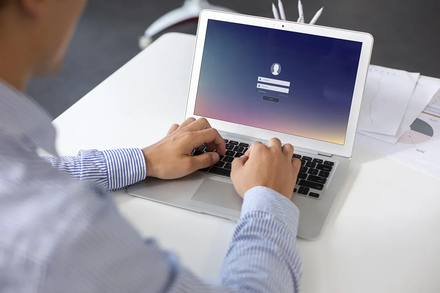 Person typing on a MacBook laptop with a login screen visible.