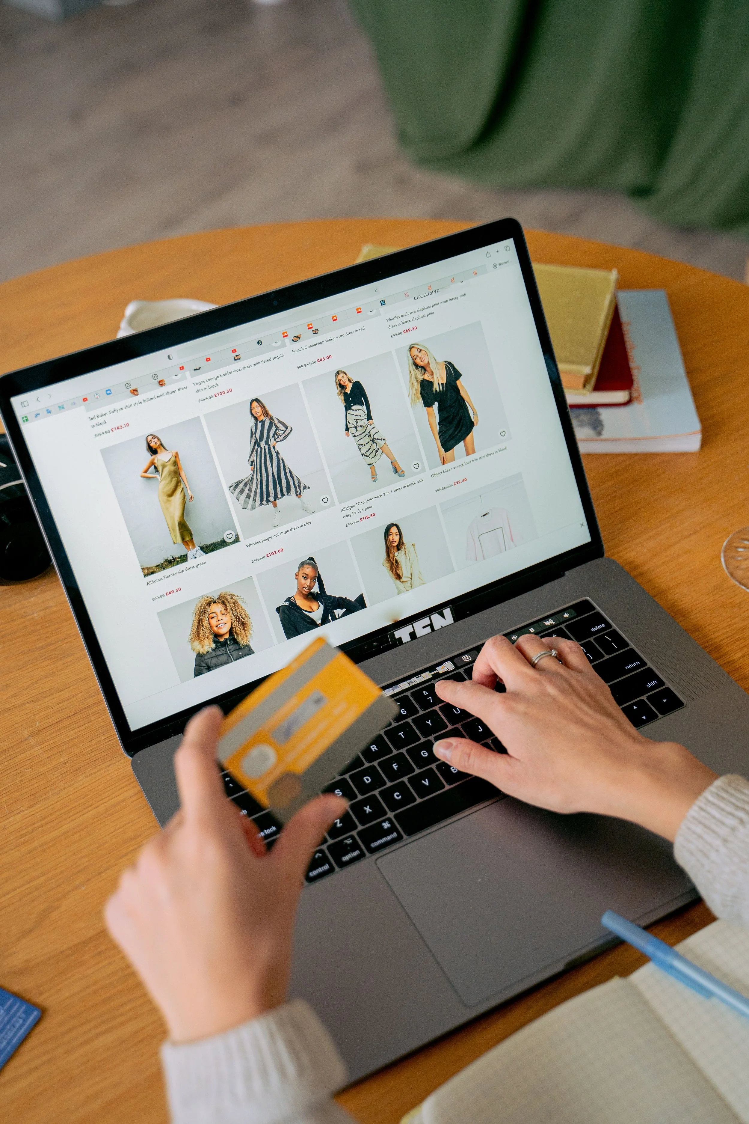 A person holds a bank card while browsing a clothing website on a laptop, ready to make a purchase.