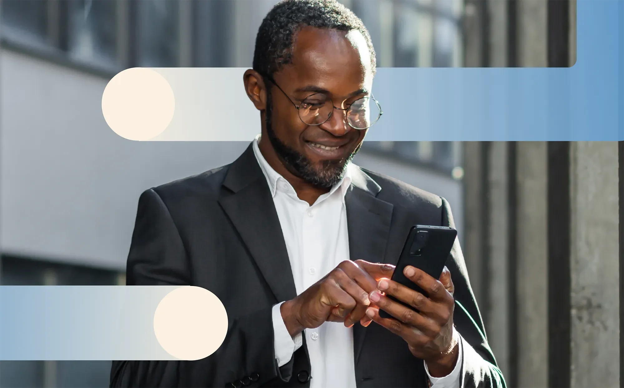 A man in a business suit looking at his phone while standing outside, smiling.