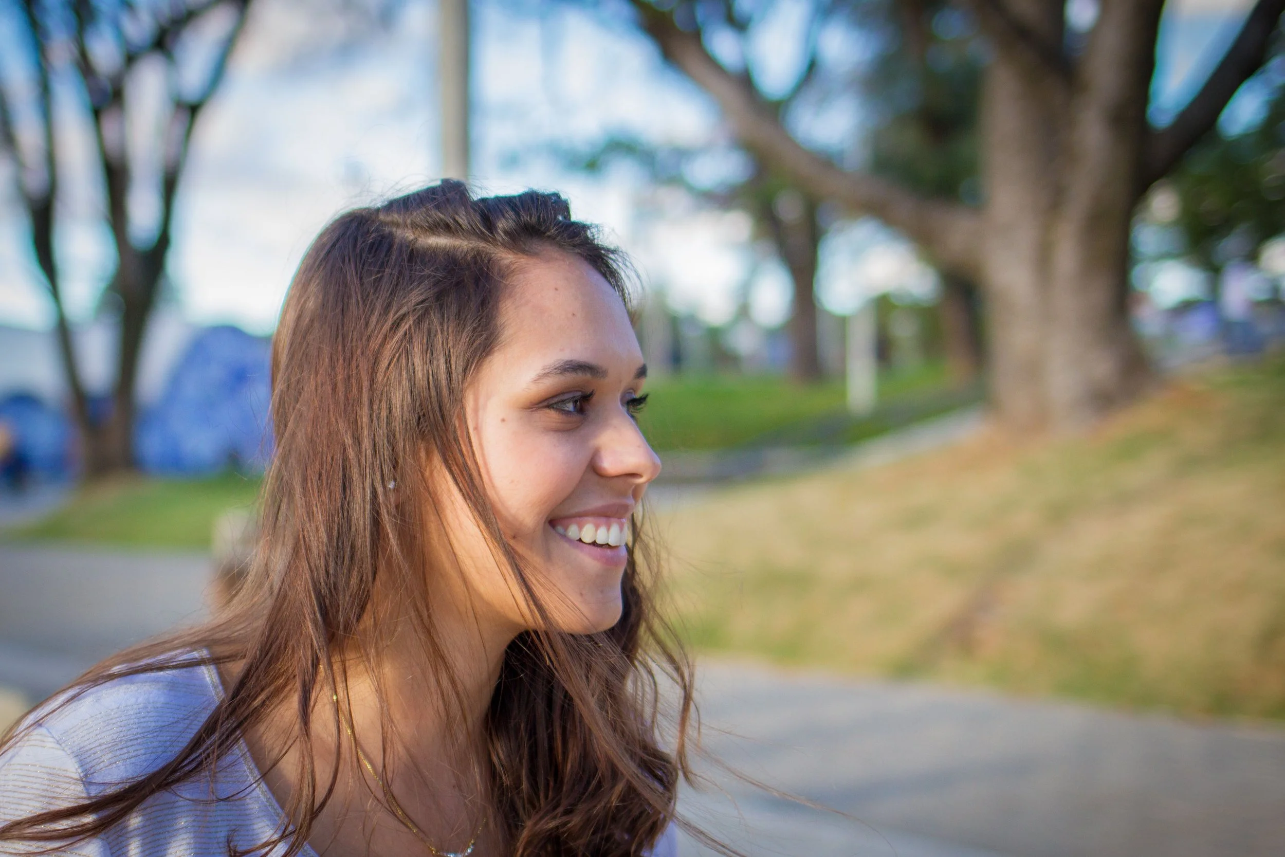 A woman smiles in a park and looks to her right.
