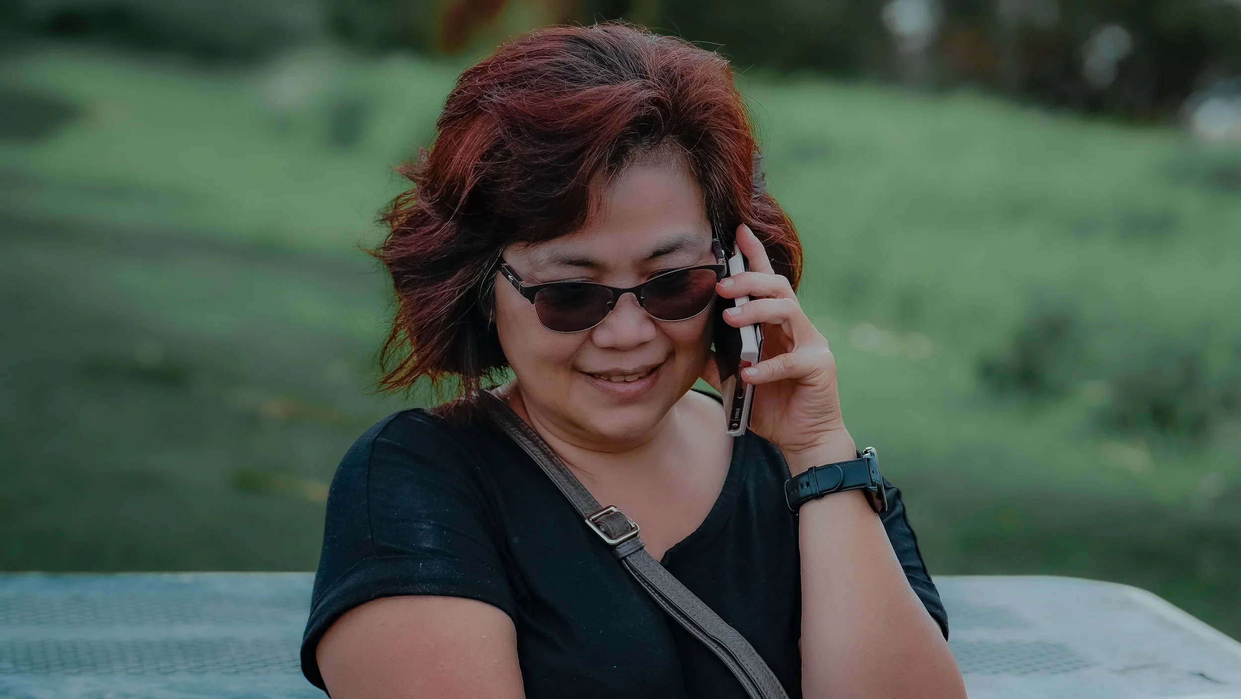 Image 1: A smiling woman with red hair and sunglasses talks on a phone outdoors, with a green park behind her.
