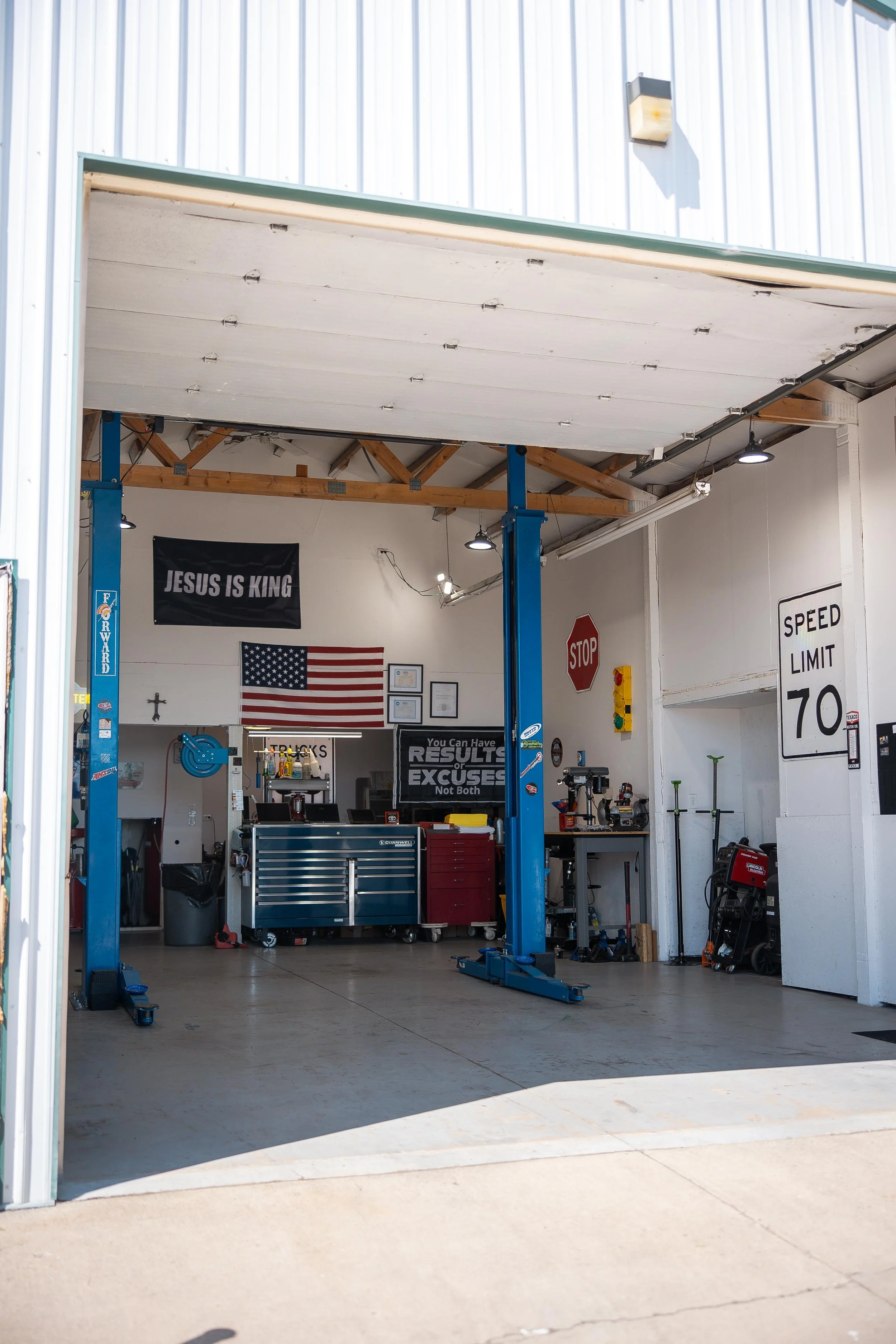 View of an automotive repair shop with a vehicle lift, tools, and American flags on the wall.