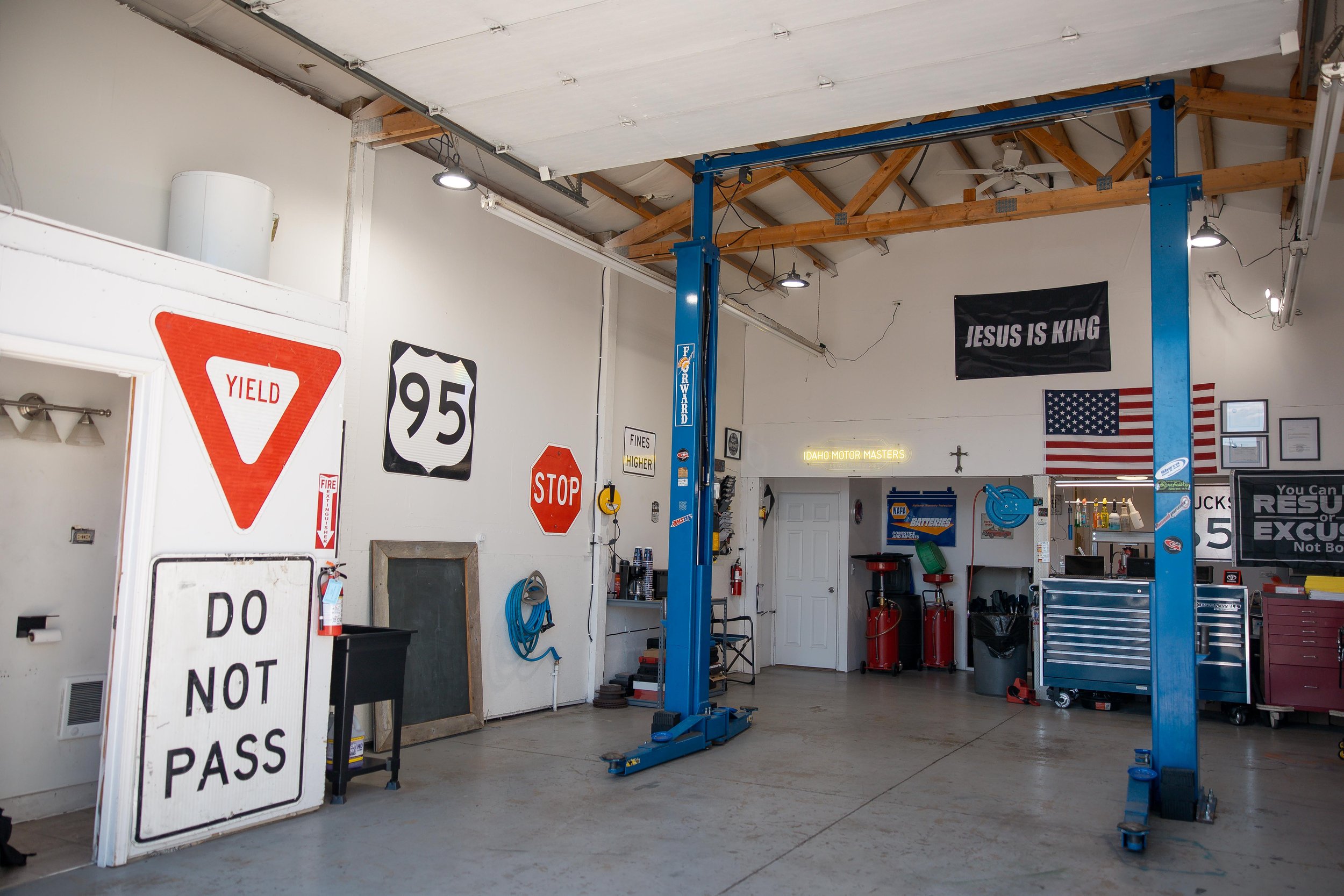Inside an auto repair shop with a blue hydraulic lift, traffic signs on the wall, and tools and equipment on display.