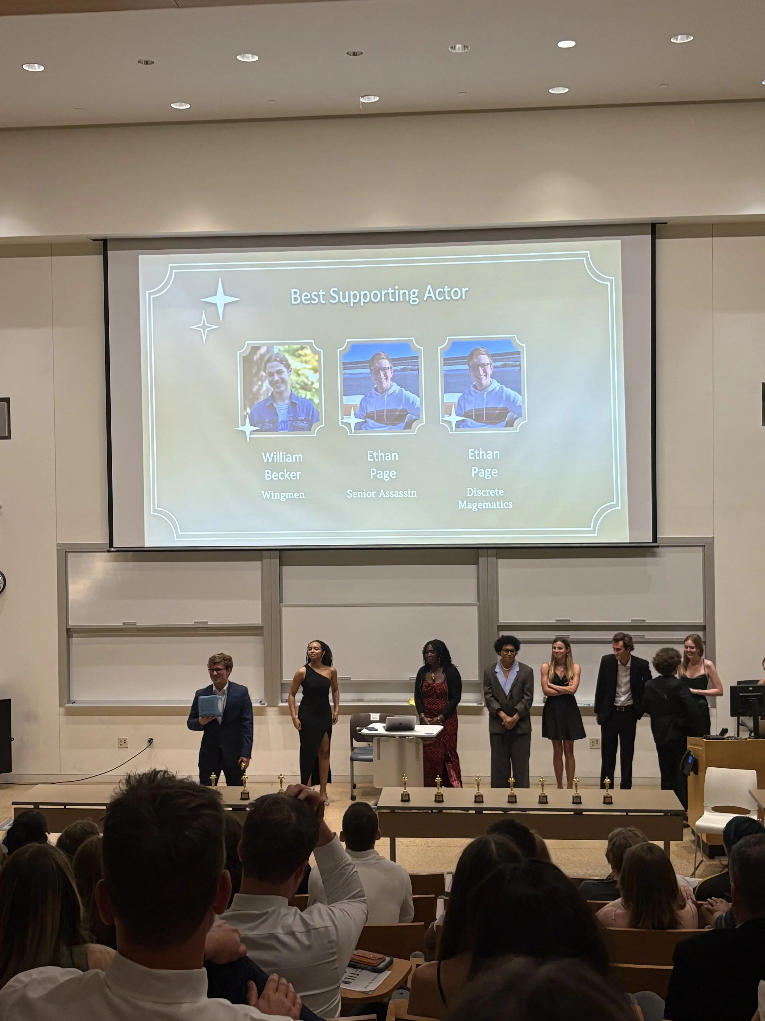 Carolina Film Association standing on stage in front of an audience for a University of North Carolina at Chapel Hill film festival with a large screen displaying award nominees and winners, including Ethan Page.