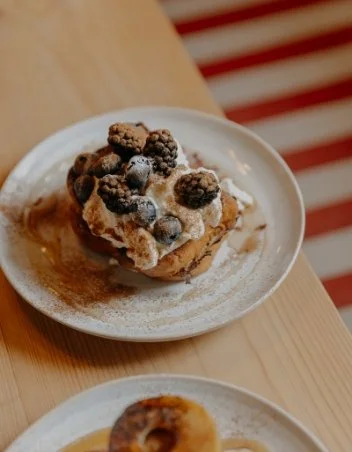 A bowl of ice cream topped with crumble and berries on a white plate, placed on a wooden table.