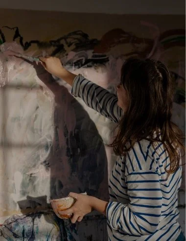 Girl painting on a large canvas with brushes and a palette.