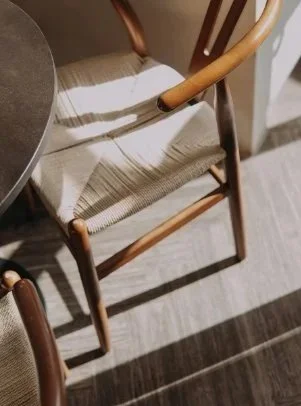 A wooden chair with a woven seat and curved armrests, positioned next to a round table in a room with striped flooring.