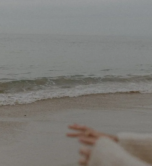 A person on a beach making a peace sign with their hand, ocean waves in the background.