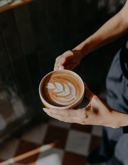 Person holding a latte with latte art in a ceramic cup.