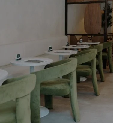 A row of green velvet chairs and white tables with electronic devices in a modern cafe or restaurant setting.